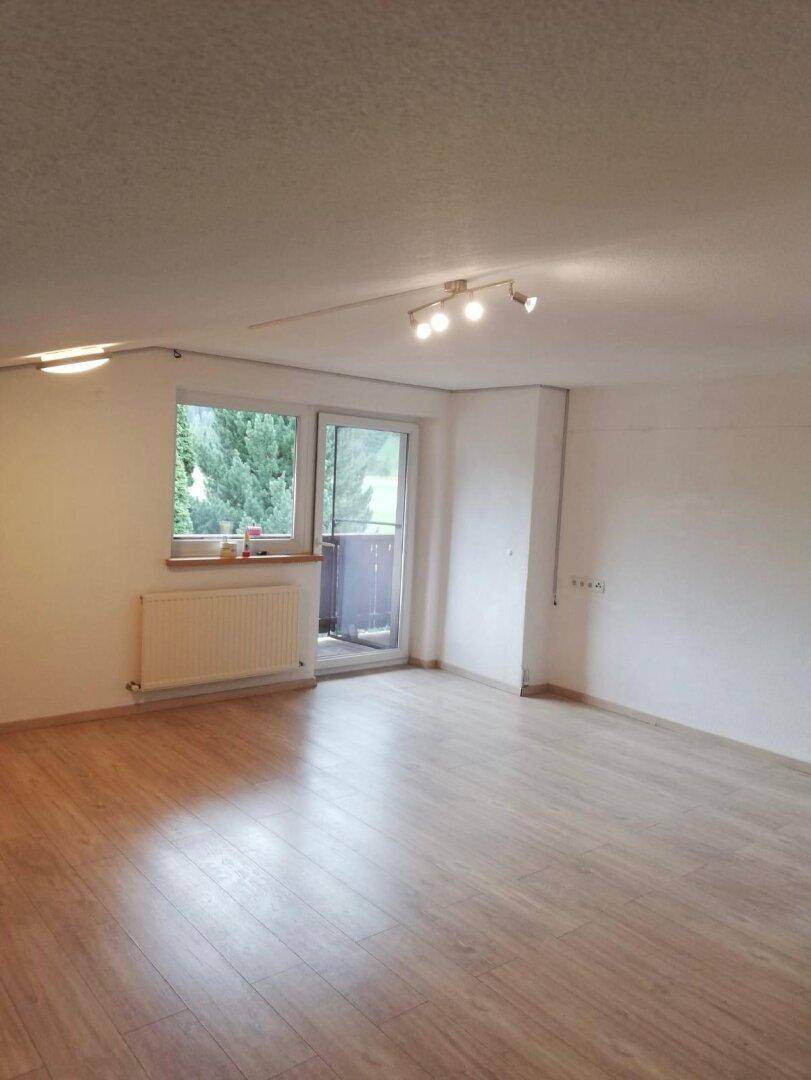 Heller, leerer Raum mit Laminatboden, Fenster und Zugang zu einem kleinen Balkon.