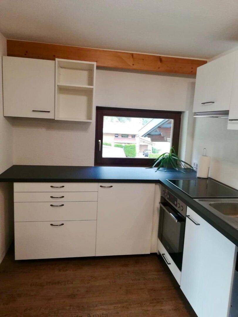 Kleine, moderne Küche mit weißen Schränken, dunkler Arbeitsplatte und integriertem Herd.