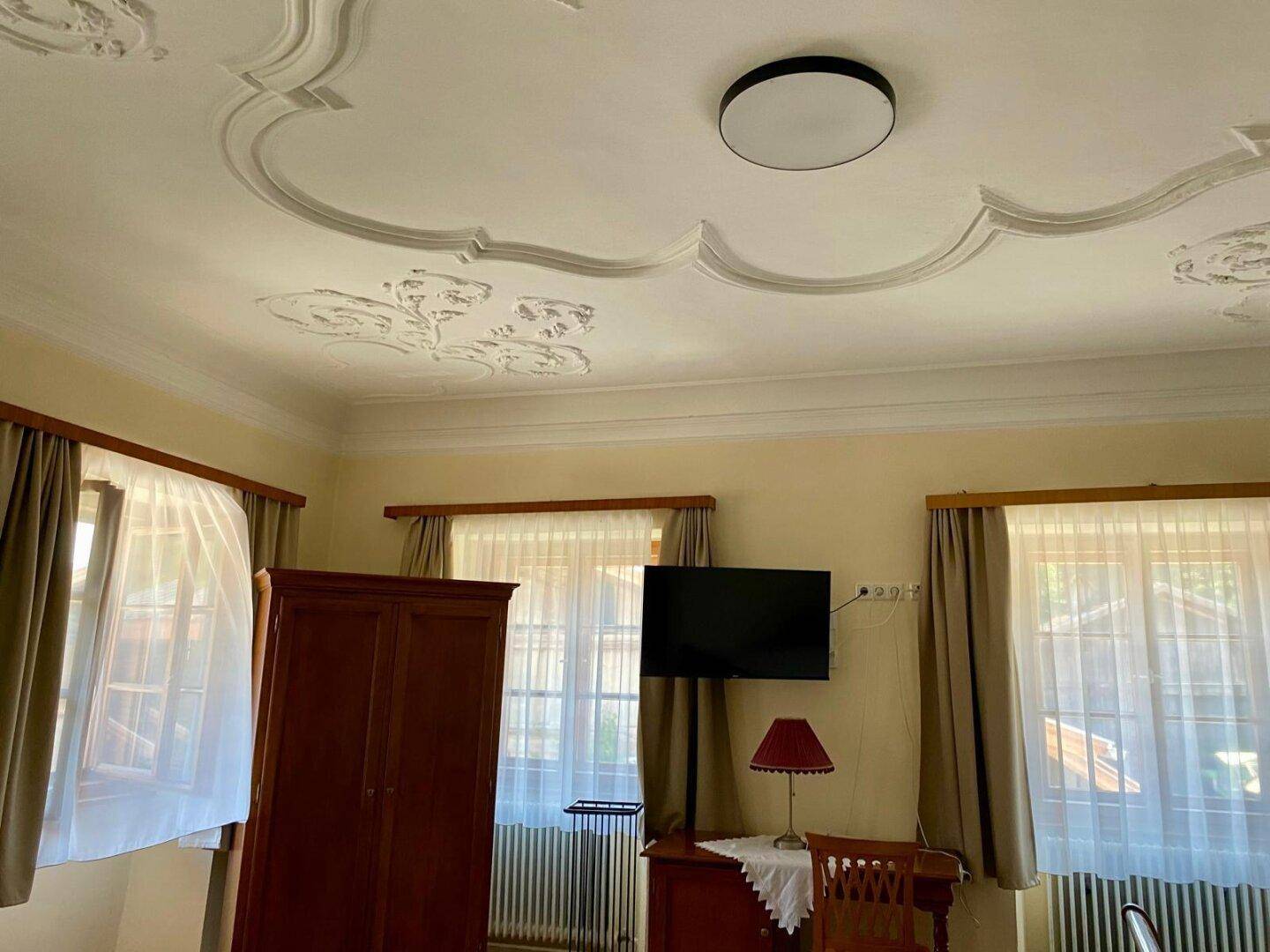 Schlafzimmer mit Stuckdecke, Holzschrank und Fernseher, der an der Wand montiert ist.