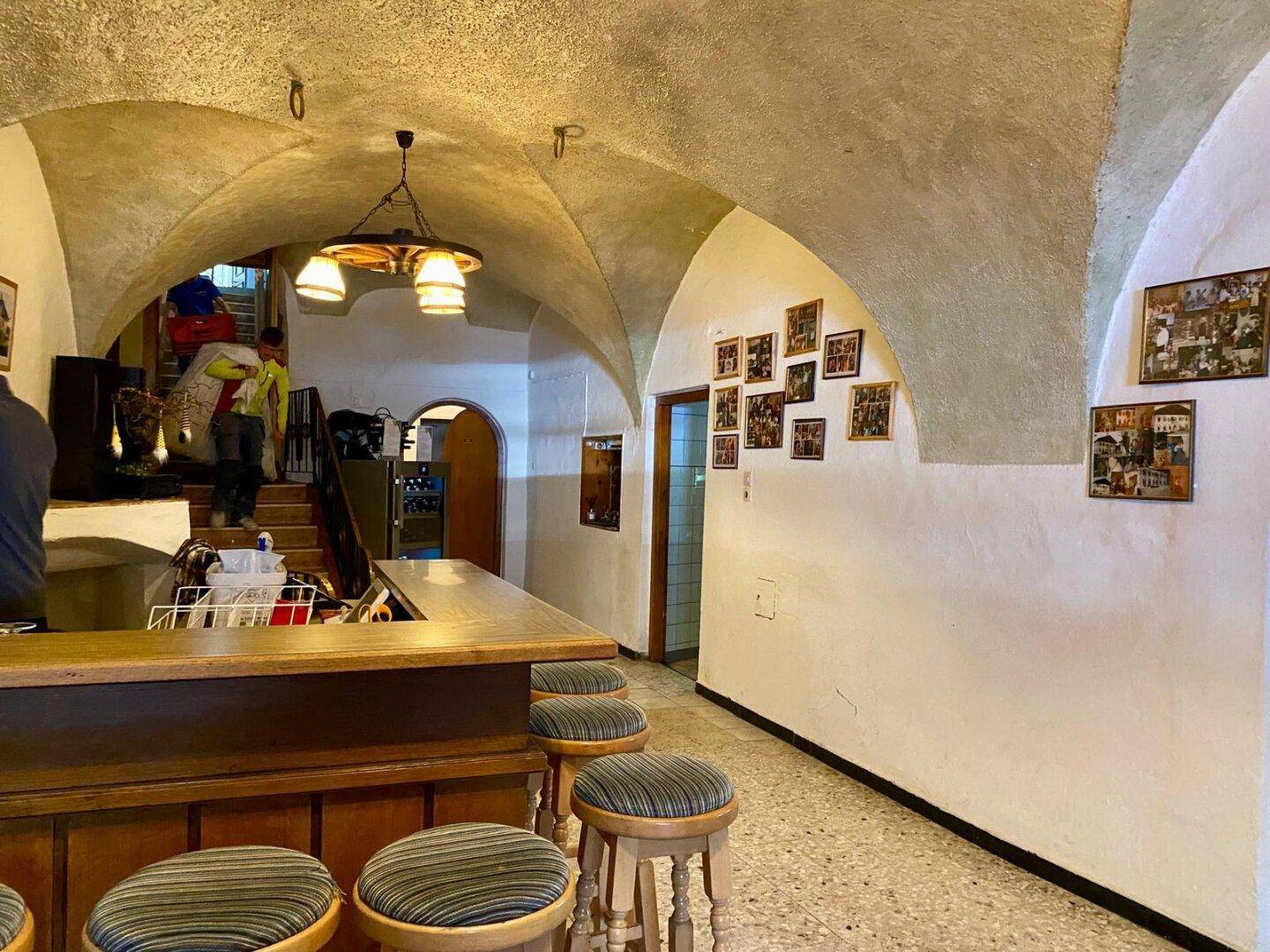 Rustikale Bar mit gewölbter Decke, Holztheke und Barhockern, die eine gemütliche Atmosphäre schafft.