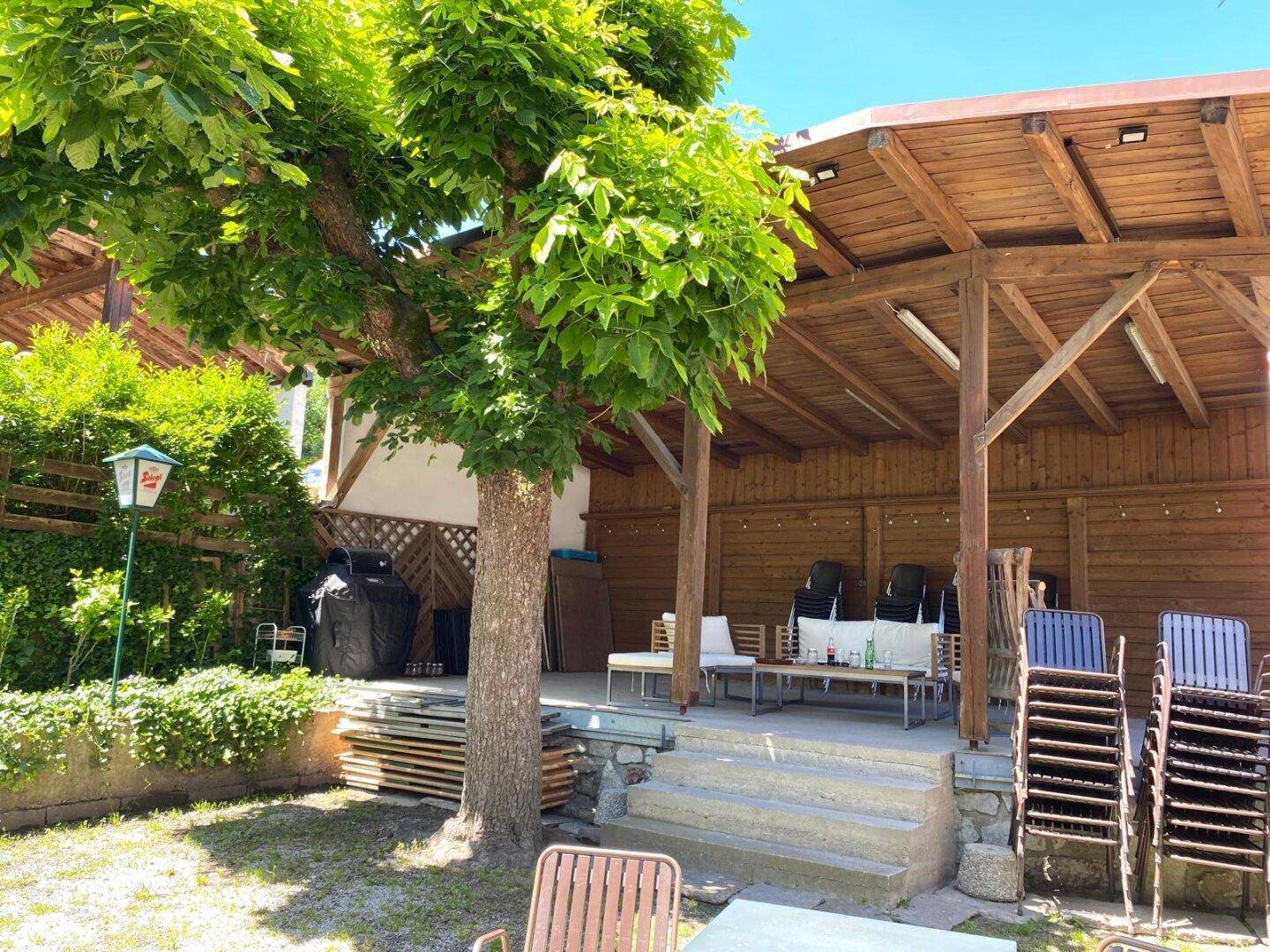 Überdachte Holzterrasse im Garten mit Stühlen und Tischen, ideal für gesellige Stunden im Freien.