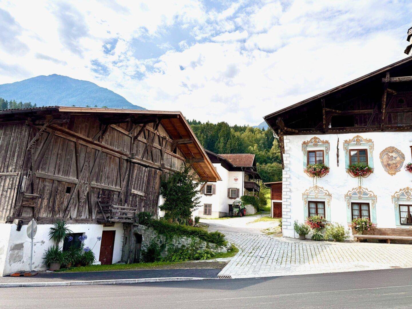 Zwei traditionelle Gebäude in einer ländlichen Umgebung mit Kopfsteinpflaster und Bergblick.