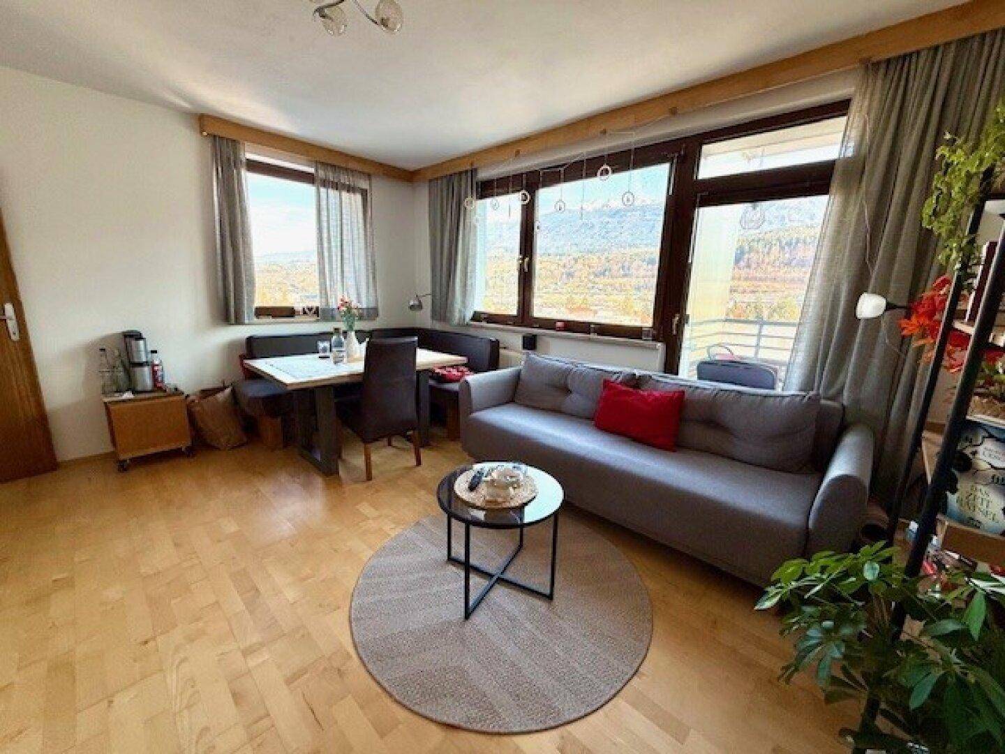 Gemütlicher Wohn-Essbereich mit Sofa, Esstisch und großen Fenstern mit Bergblick.