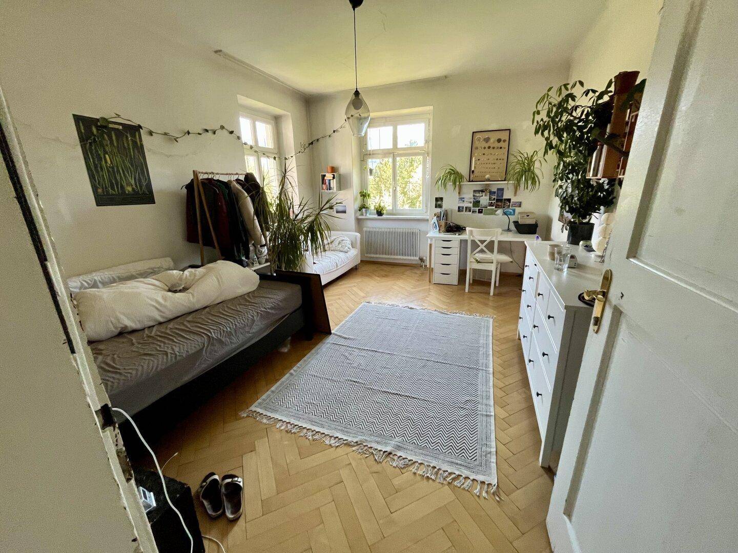 Helles Schlafzimmer mit zwei Betten, Parkettboden und viel Tageslicht.