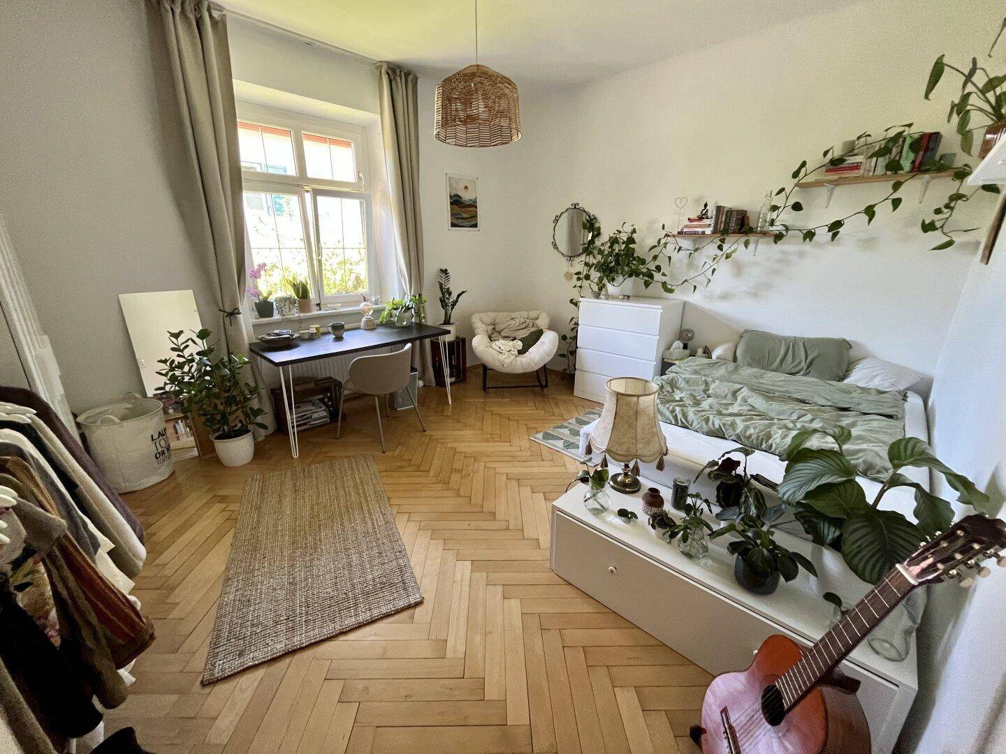 Helles Schlafzimmer mit Parkettboden, vielen Pflanzen und einem Schreibtisch.