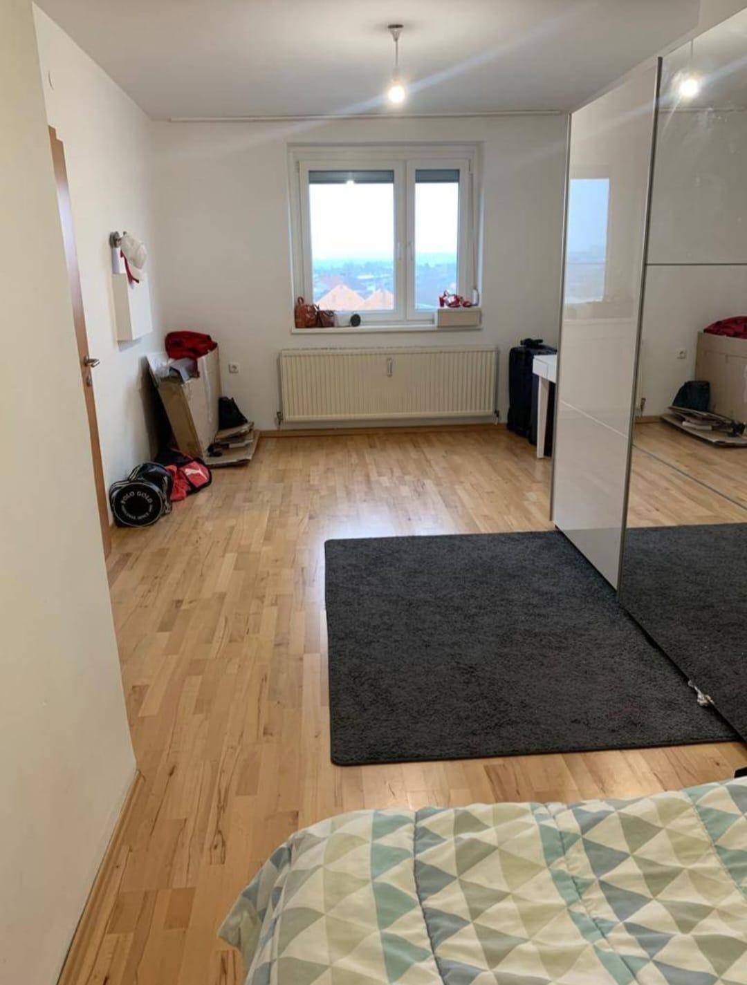 Helles Schlafzimmer mit Holzboden, Fenster und Heizkörper.