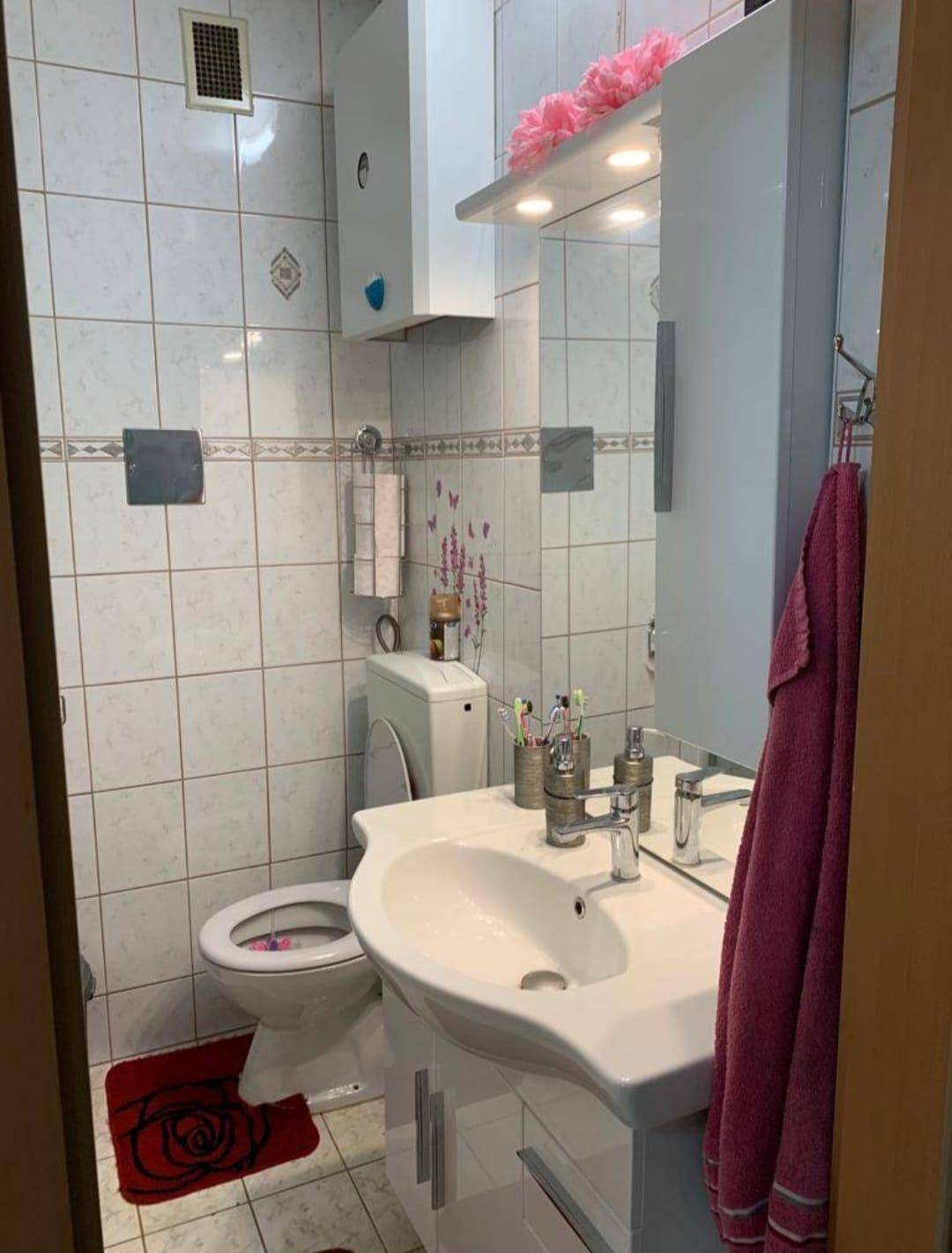 Badezimmer mit WC, Waschbecken, Spiegelschrank und weißen Fliesen.