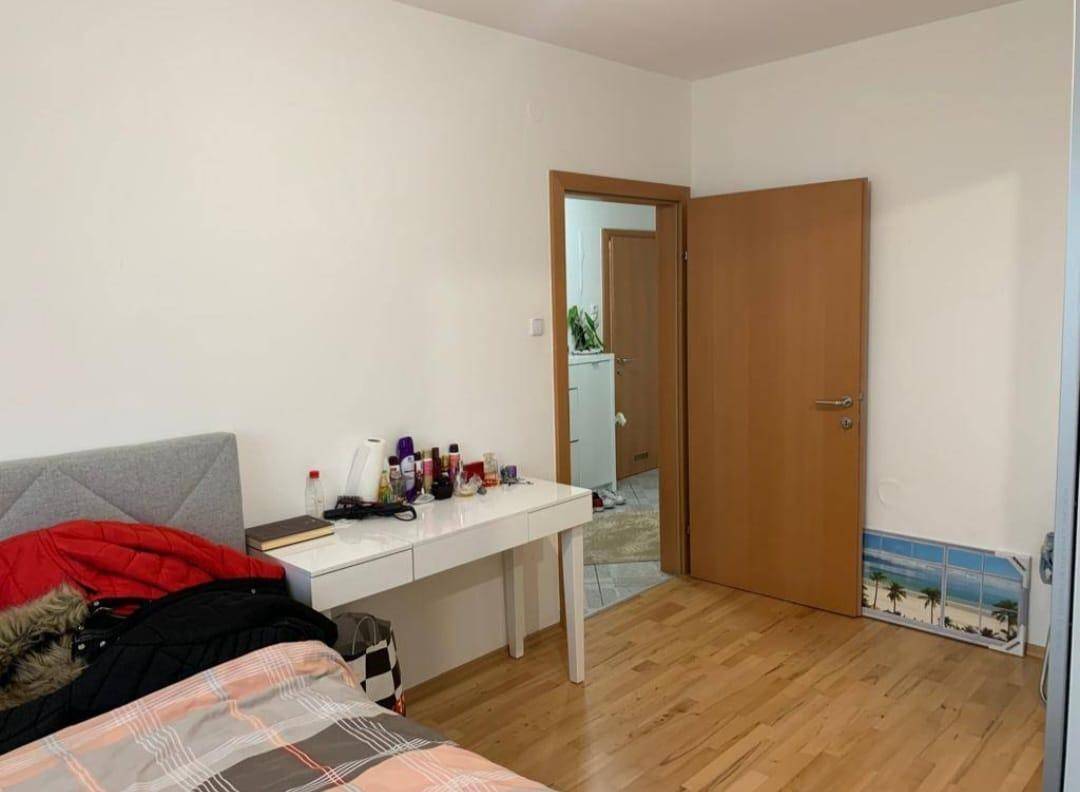 Schlafzimmer mit Holzboden, Schreibtisch und Zugang zu einem weiteren Raum.