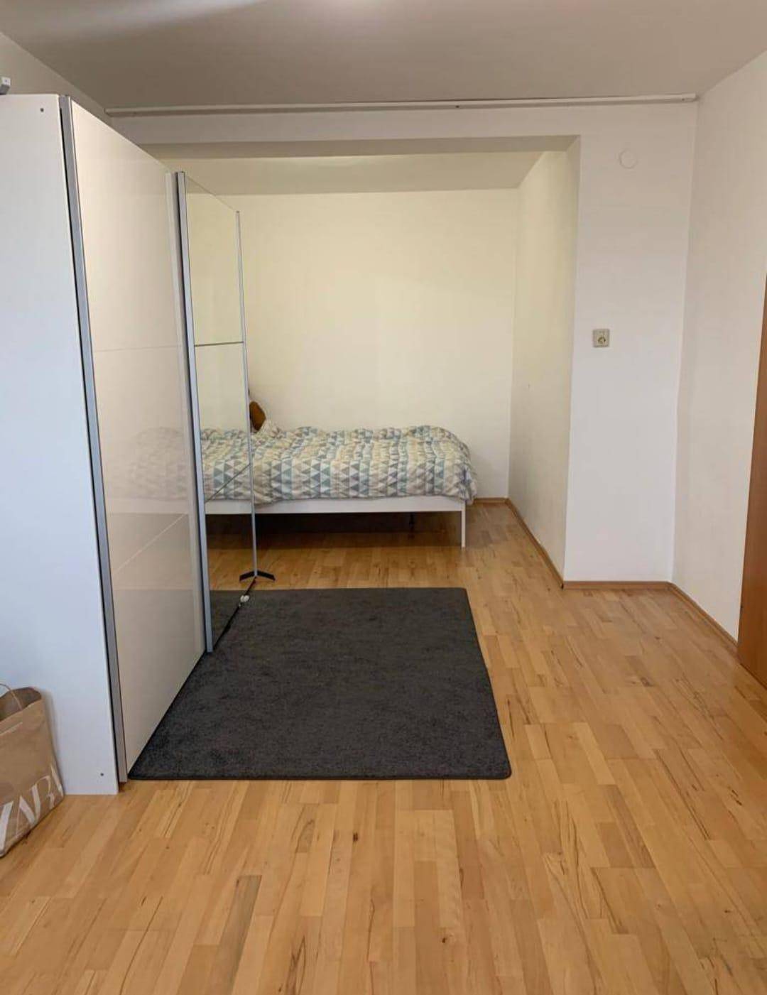 Schlafzimmer mit Bett in Nische, Spiegelschrank und Holzboden.