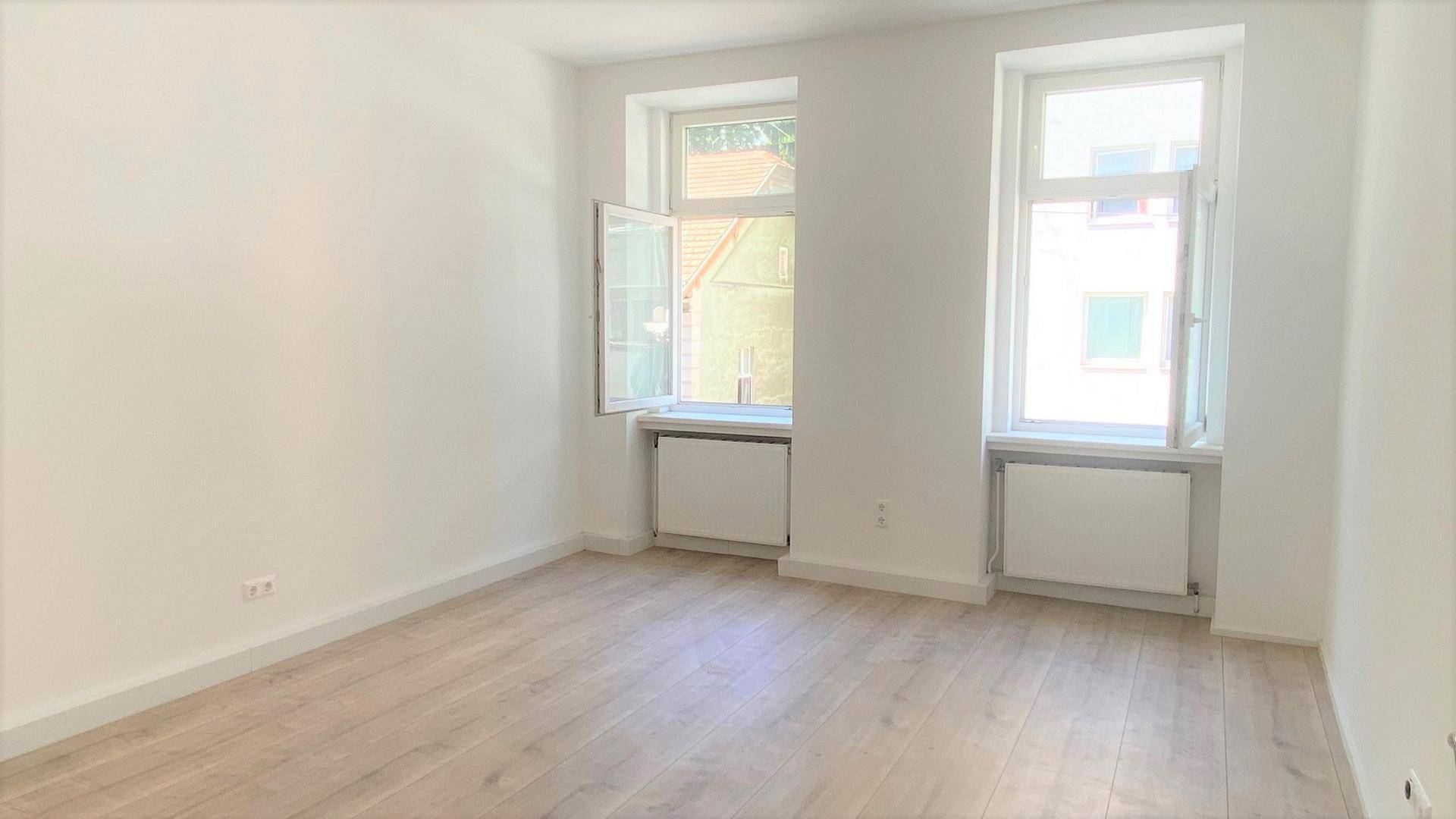 Lichtdurchflutetes Zimmer mit geöffneten Fenstern und hellem Holzboden, bereit zur Einrichtung.