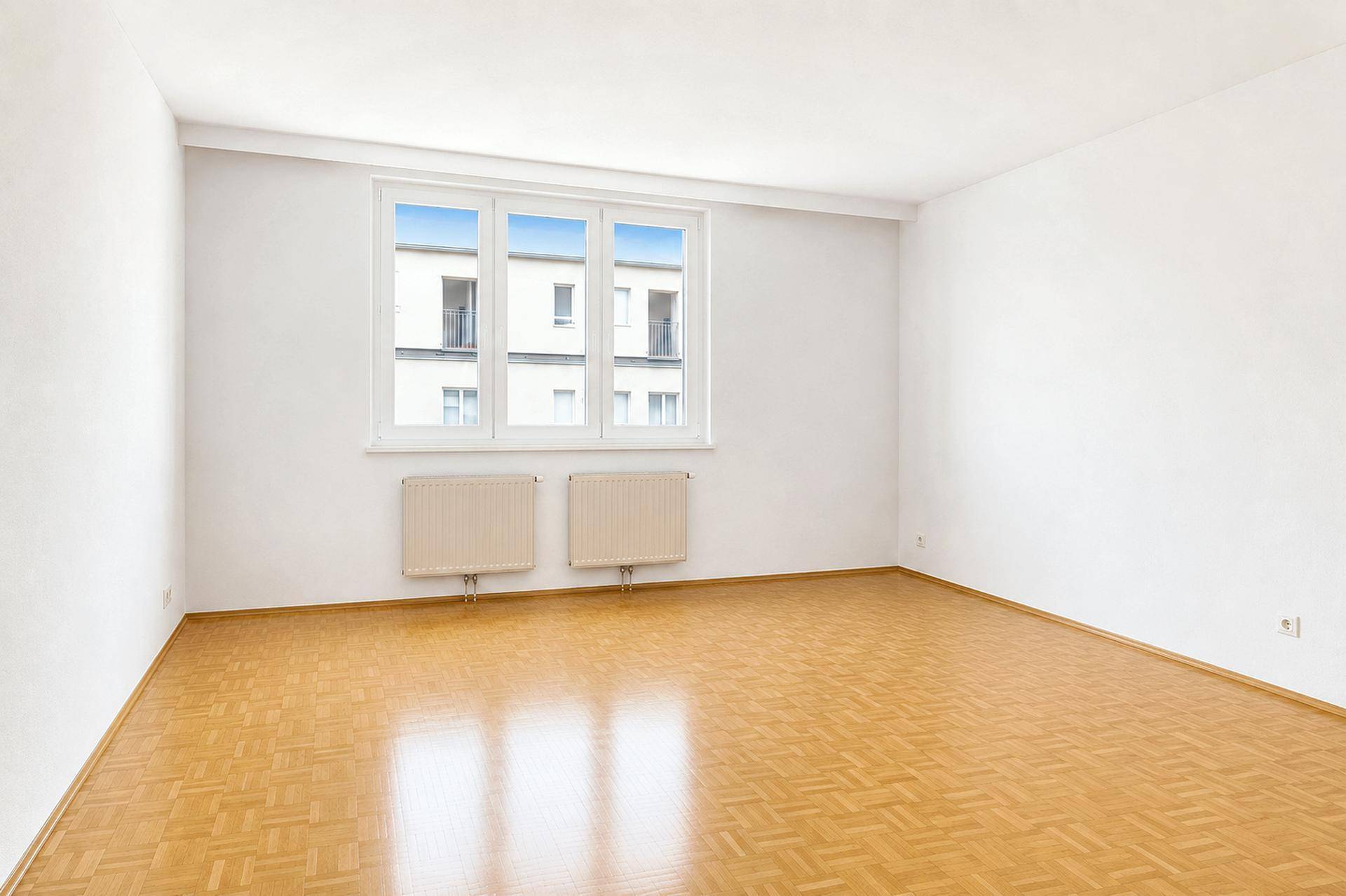 Heller, leerer Raum mit Parkettboden, großen Fenstern und Heizkörpern, bereit zur individuellen Einrichtung.