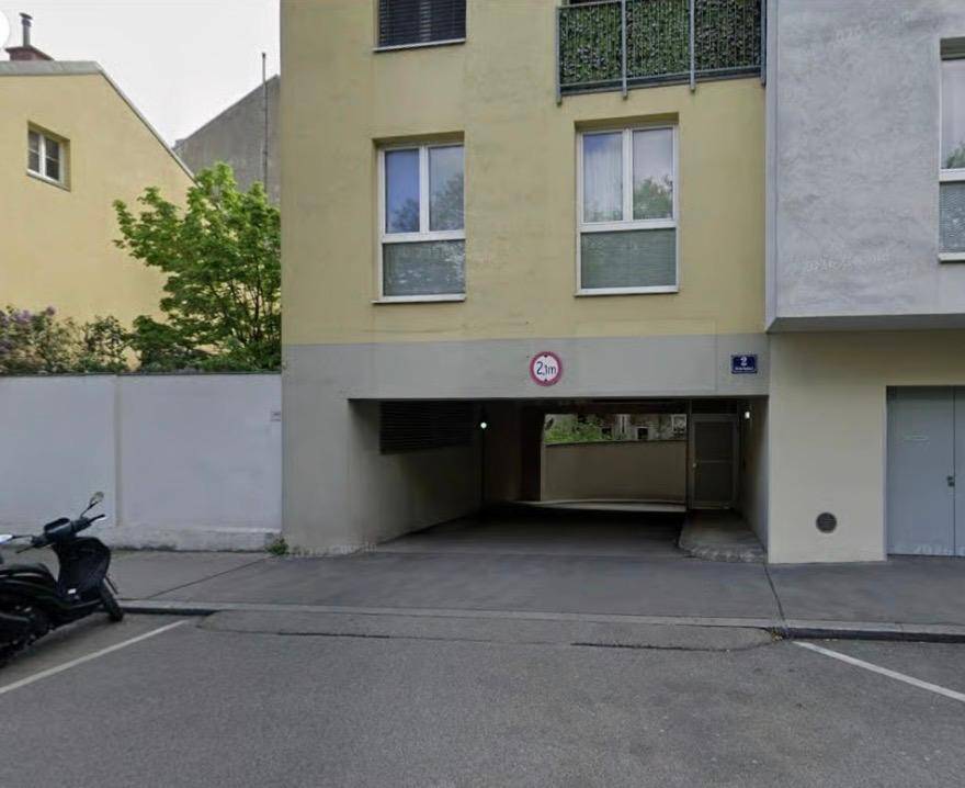 Eingang zu einer Tiefgarage unter einem Wohngebäude mit Balkonen und Fenstern an der Fassade.