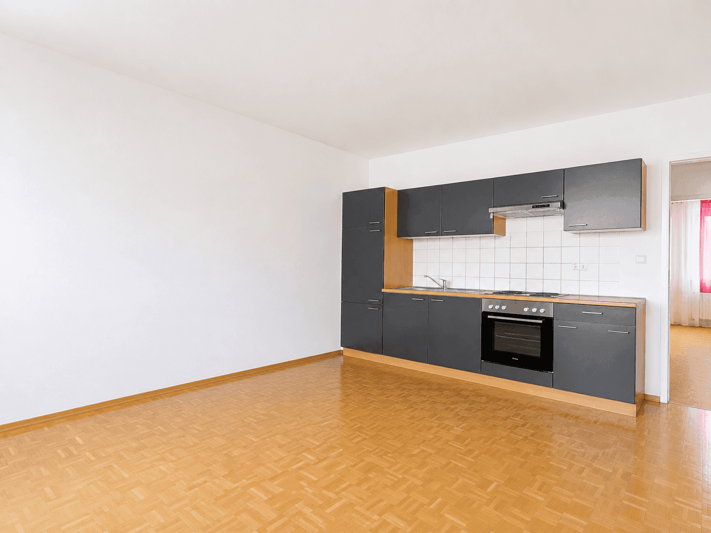 Funktionale Einbauküche mit grauen Schränken, Herd und Backofen in einem hellen Raum mit Parkettboden.