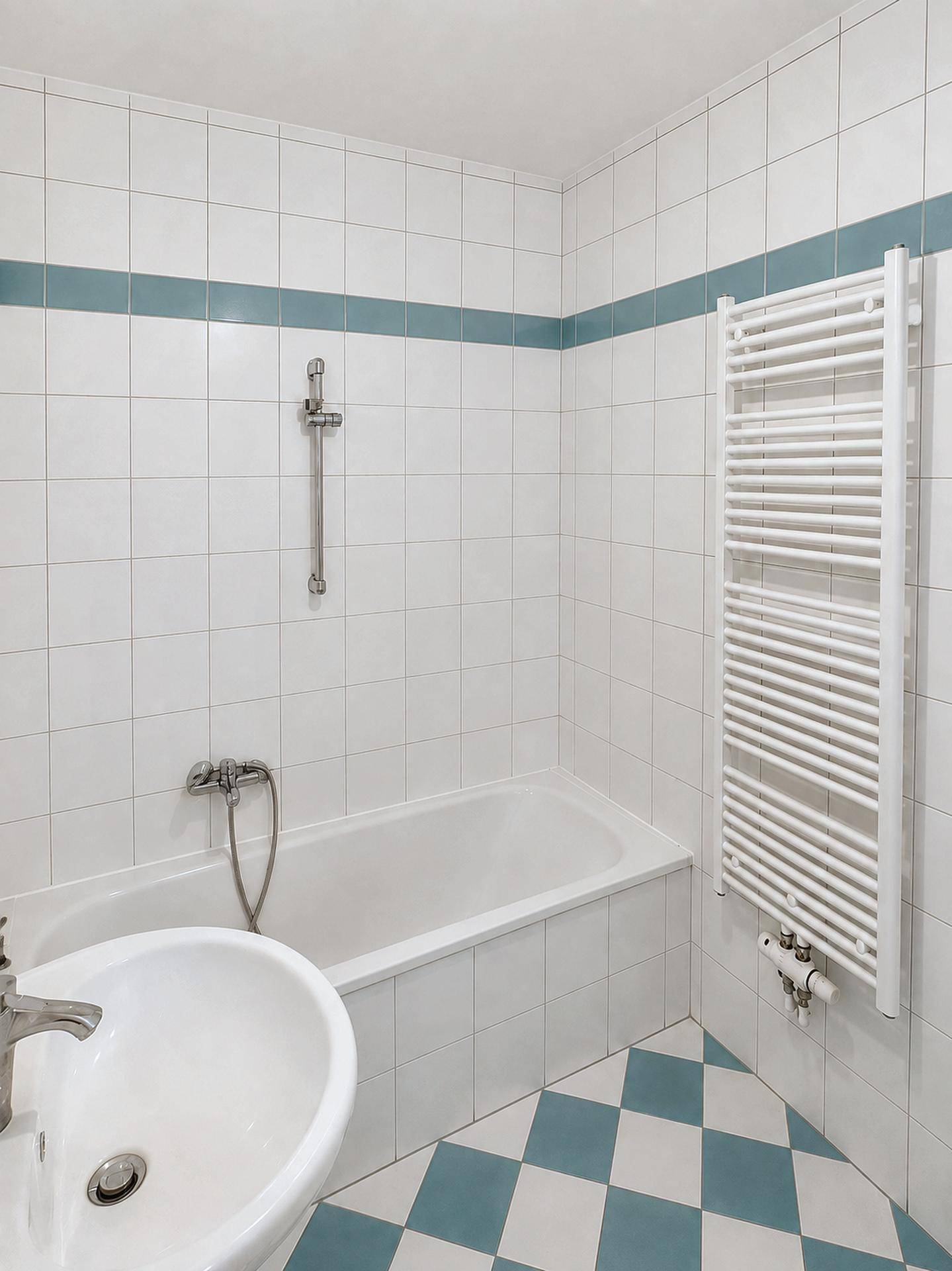 Badezimmer mit Badewanne, Waschbecken und beheiztem Handtuchhalter, gefliest in Weiß und Blau.