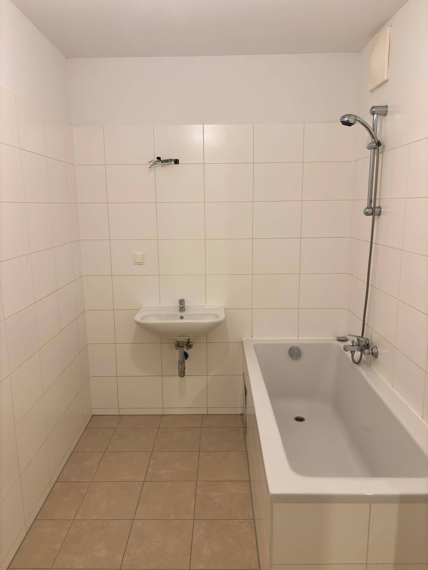 Gefliestes Badezimmer mit Badewanne, Waschbecken und Duscharmatur.