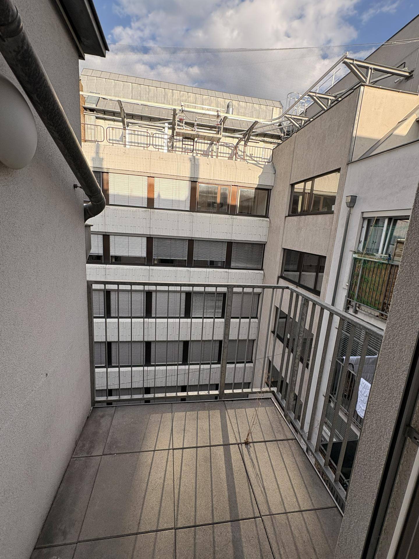 Kleiner Balkon mit Fliesenboden und Blick auf umliegende Gebäude.