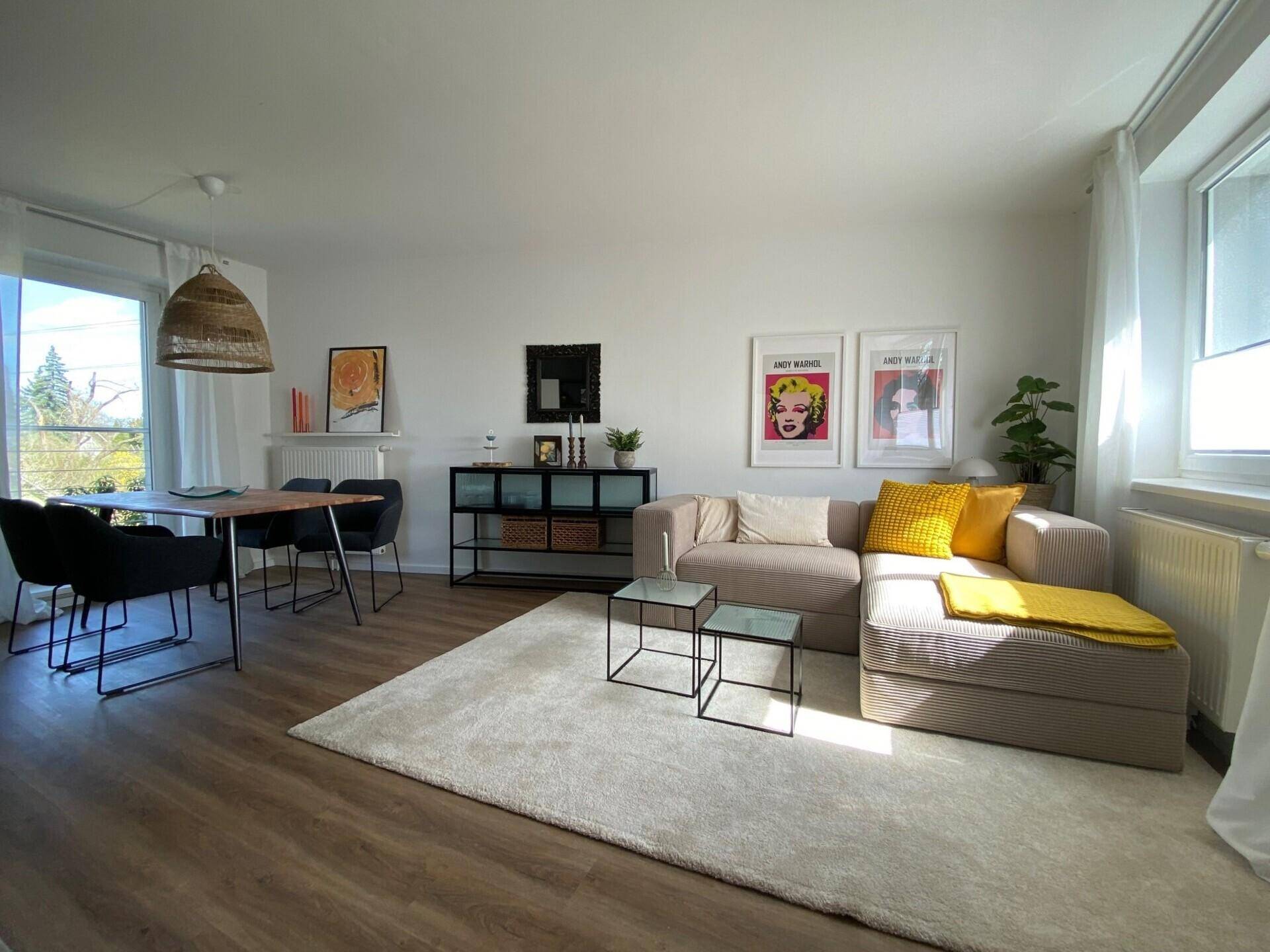 Offener Wohn- und Essbereich mit beigem Sofa, Esstisch und großen Fenstern für viel Tageslicht.