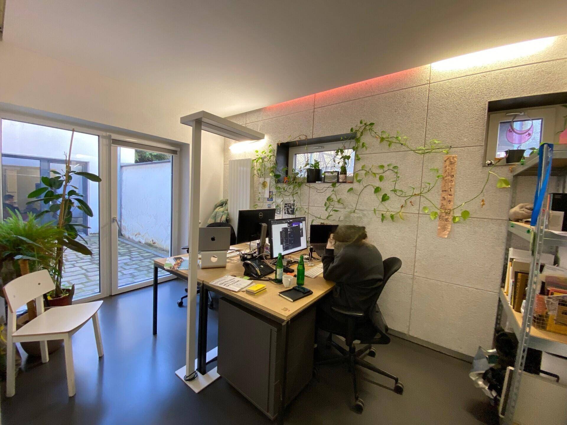 Heller Arbeitsbereich mit Schreibtisch, Pflanzen und direktem Zugang zu einem gepflasterten Außenbereich.