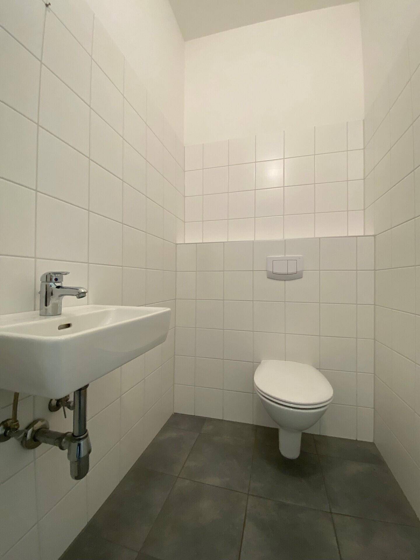 Kleines Gäste-WC mit wandhängendem WC, Waschbecken und weißen Fliesen.