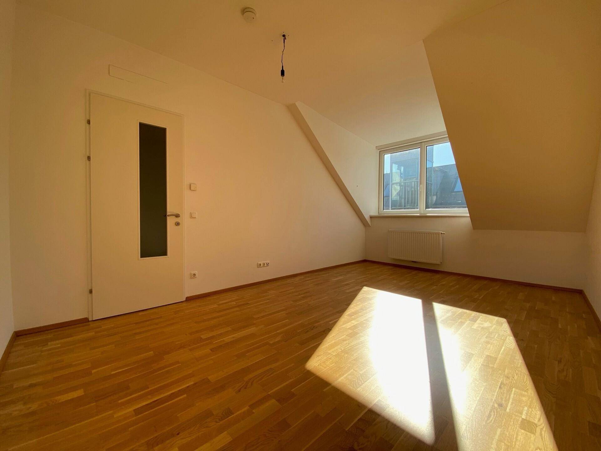 Helles Schlafzimmer in der Dachgeschosswohnung mit Holzboden, schräger Decke und viel Sonnenlicht.
