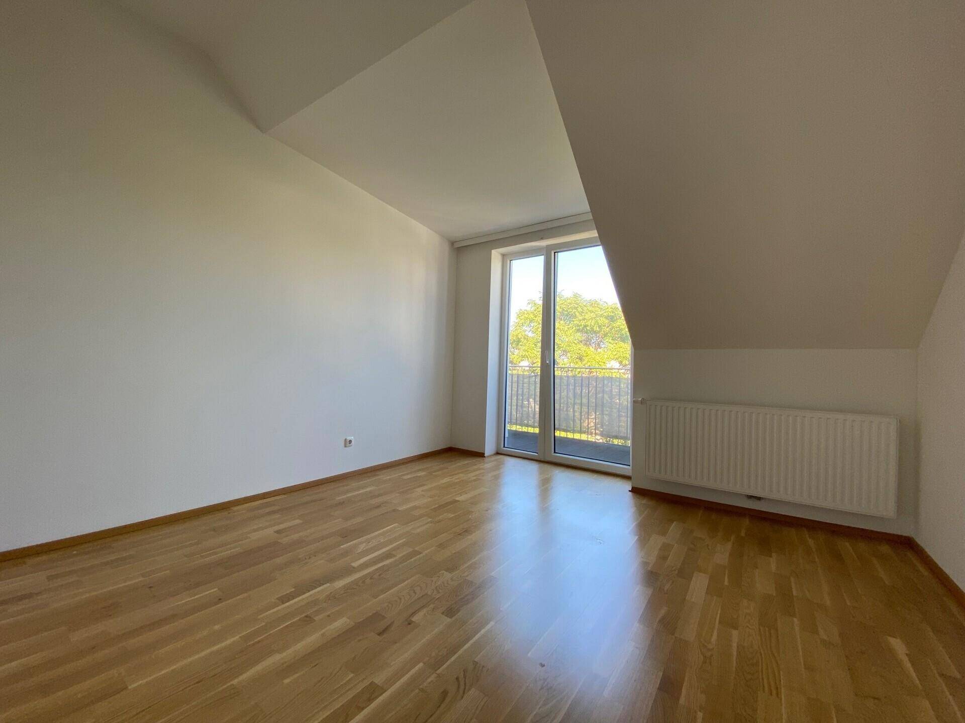 Helles Schlafzimmer mit Holzboden, schräger Decke und direktem Zugang zum Balkon.