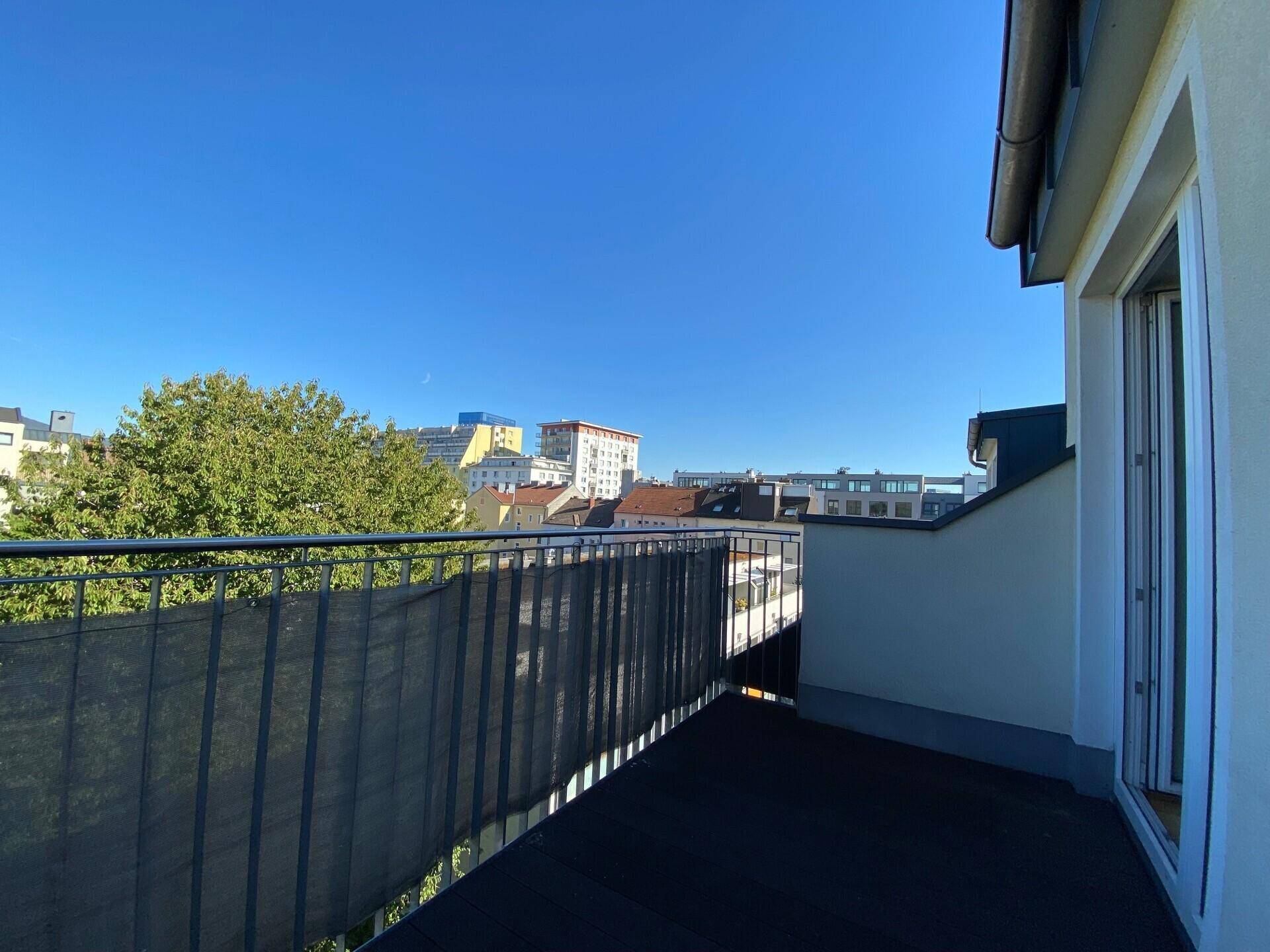 Sonniger Balkon mit Metallgeländer und Blick auf die umliegenden Gebäude und Bäume.