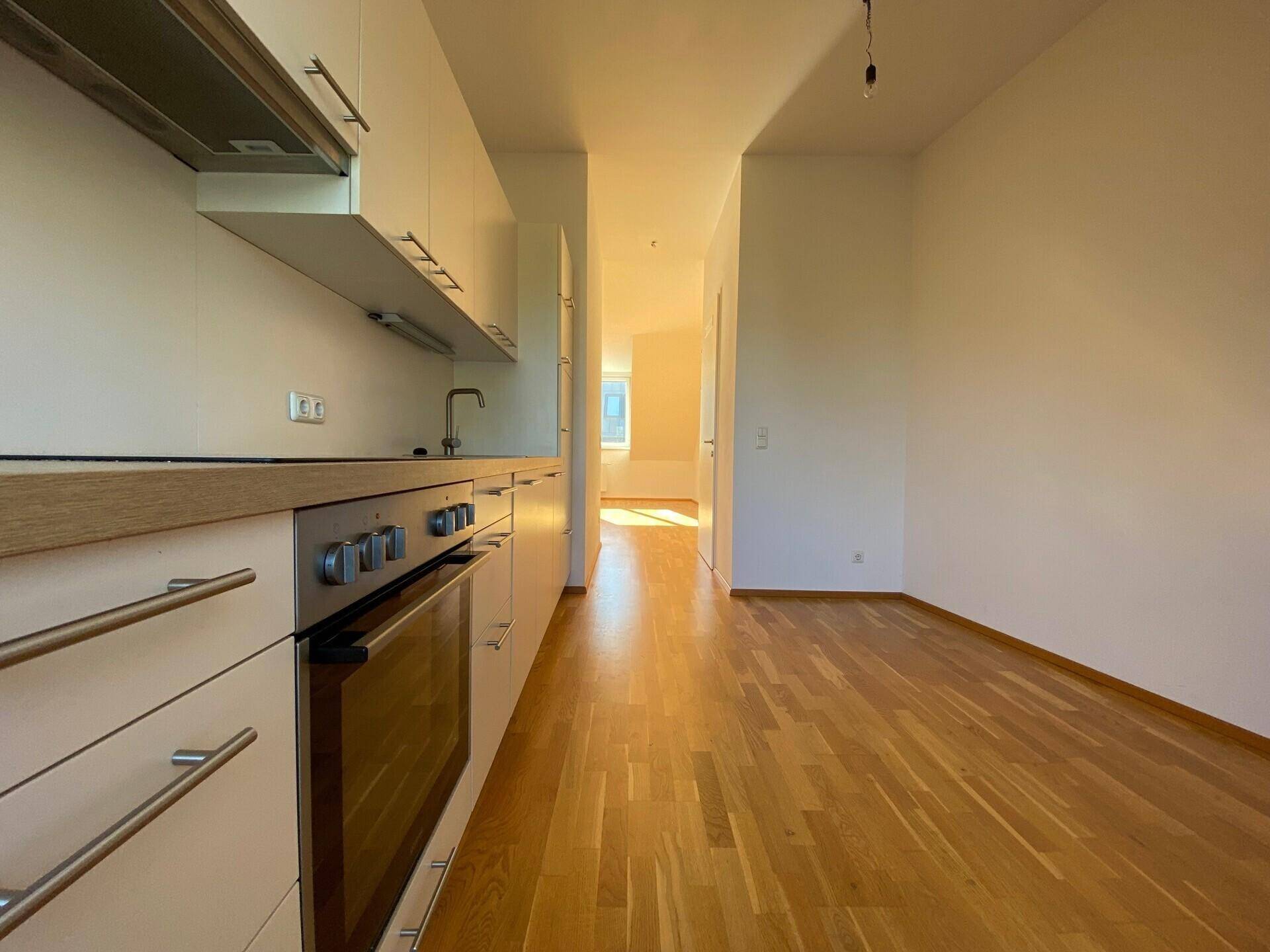 Moderne Küchenzeile mit Holzarbeitsplatte und Blick in den hellen Flur der Wohnung.
