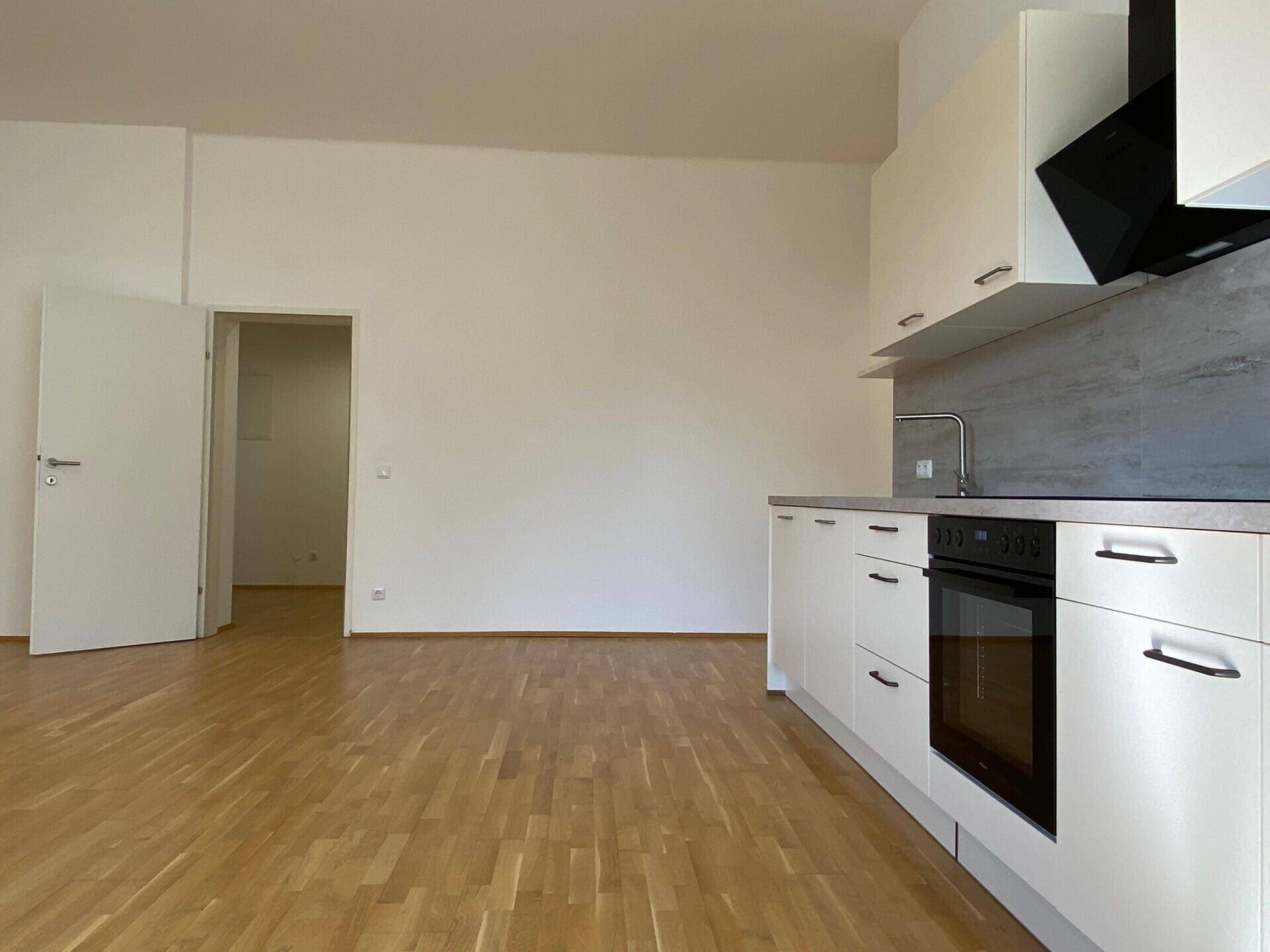 Detailansicht der modernen Küche mit Backofen, Spüle und hellen Schränken, angrenzend an einen Flur.