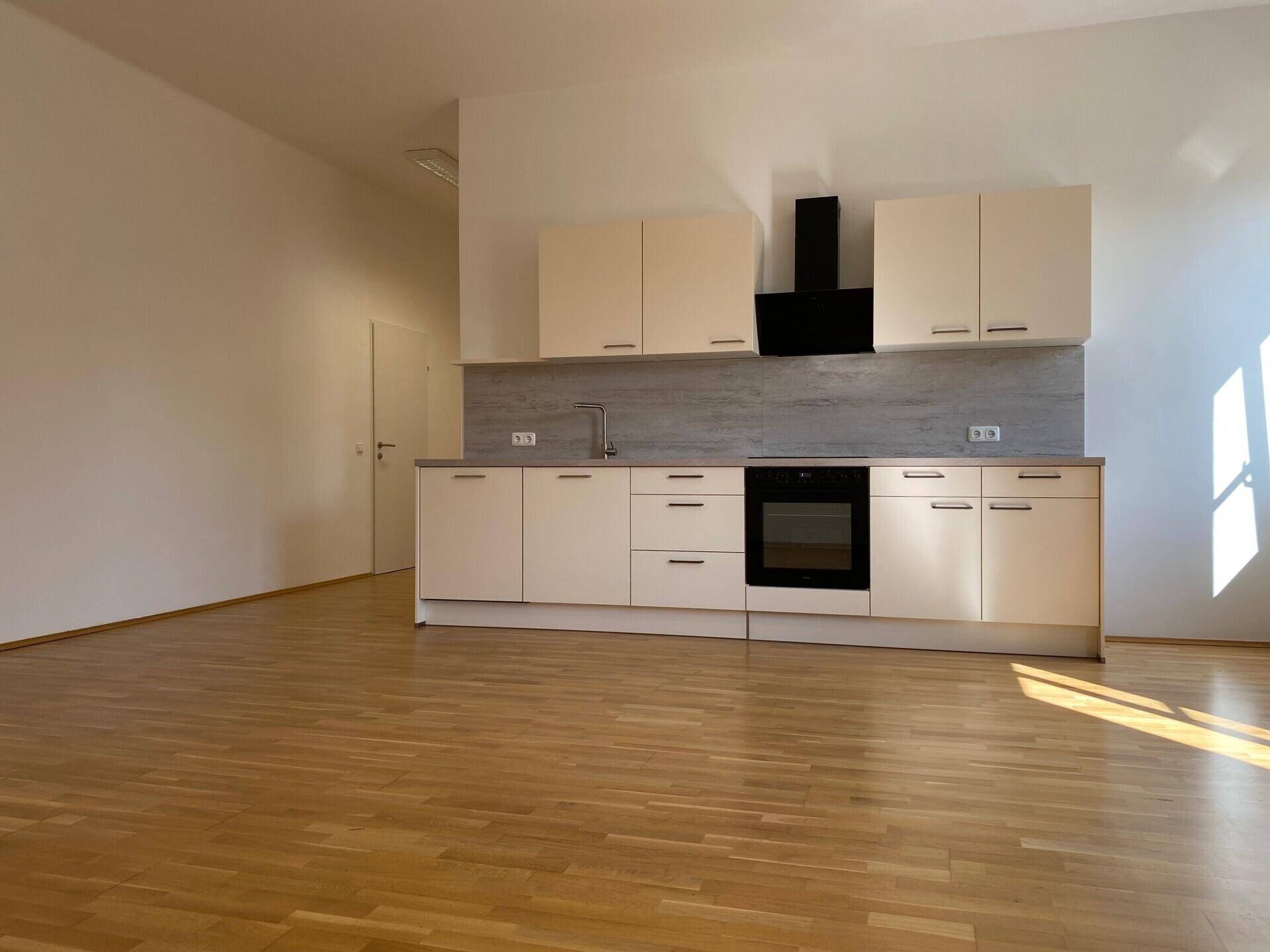Geräumige Küche mit beigen Einbauschränken und Parkettboden, offen zu einem weiteren Bereich.