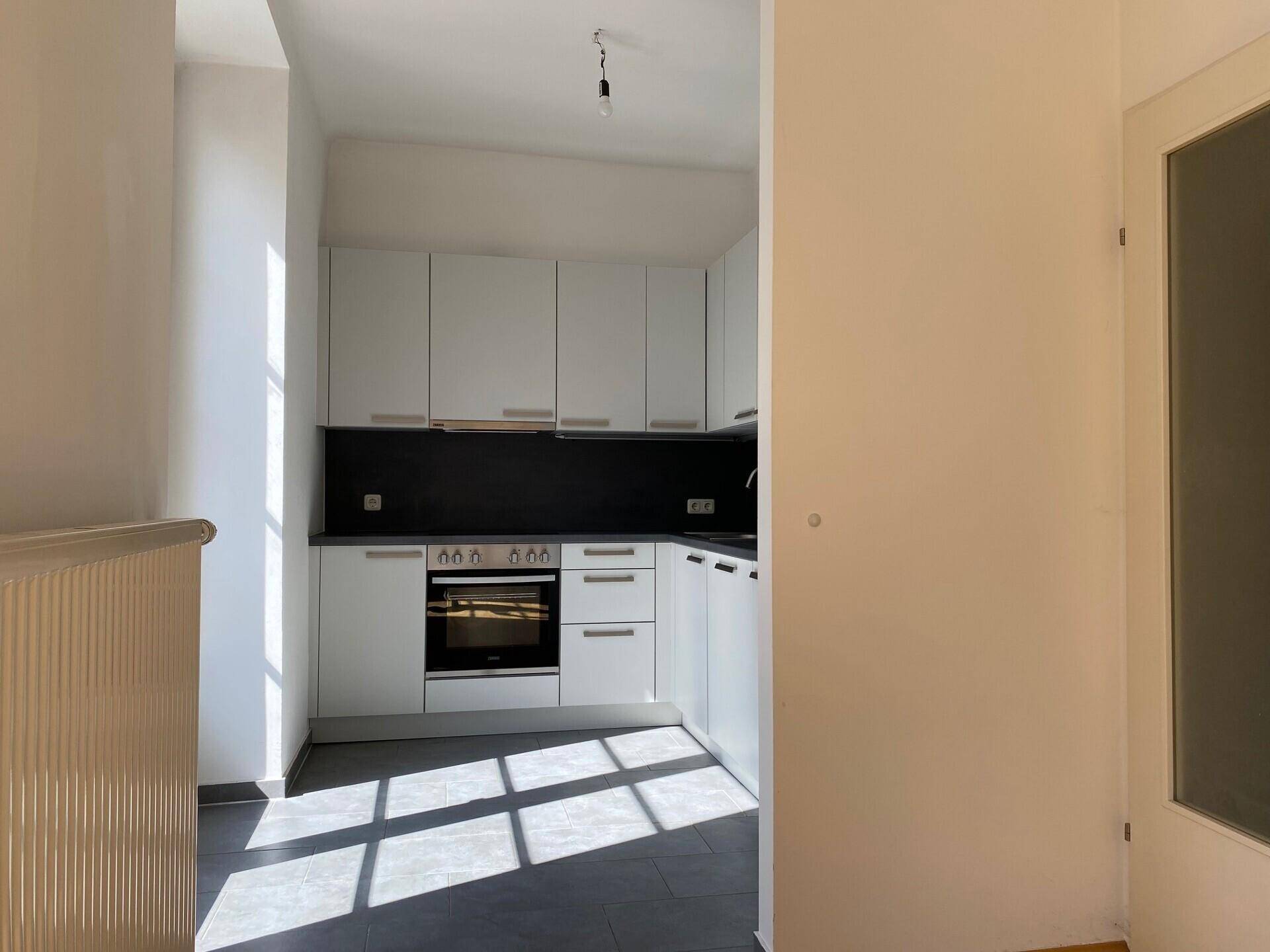 Moderne Küche mit weißen Schränken, dunkler Arbeitsplatte und Fliesenboden.