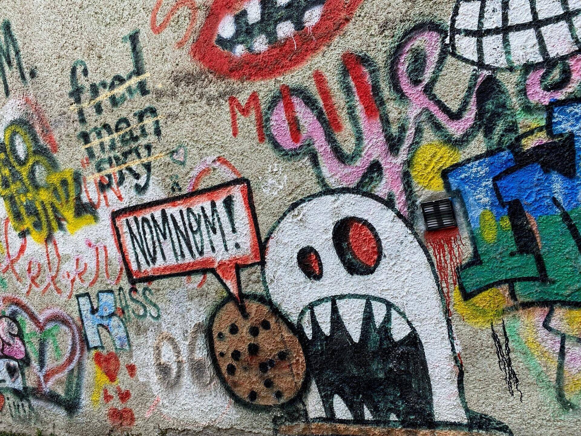 Bunte Graffiti-Kunst an einer Außenwand mit verschiedenen Motiven und Schriftzügen, die eine lebendige Atmosphäre schafft.