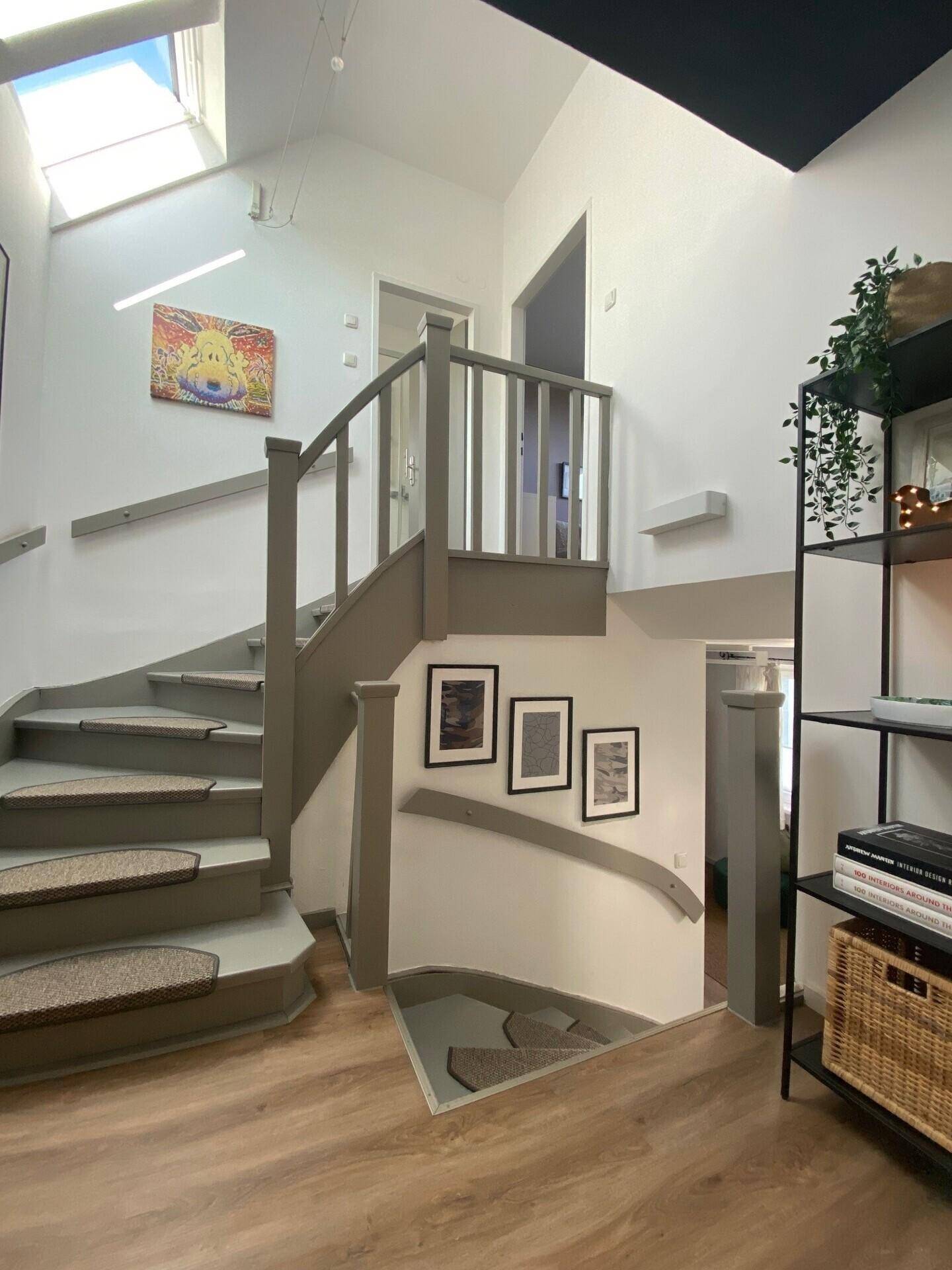 Geräumiger Flur mit Treppe, Dachfenster und einem Regal, das Pflanzen und Dekorationen trägt.