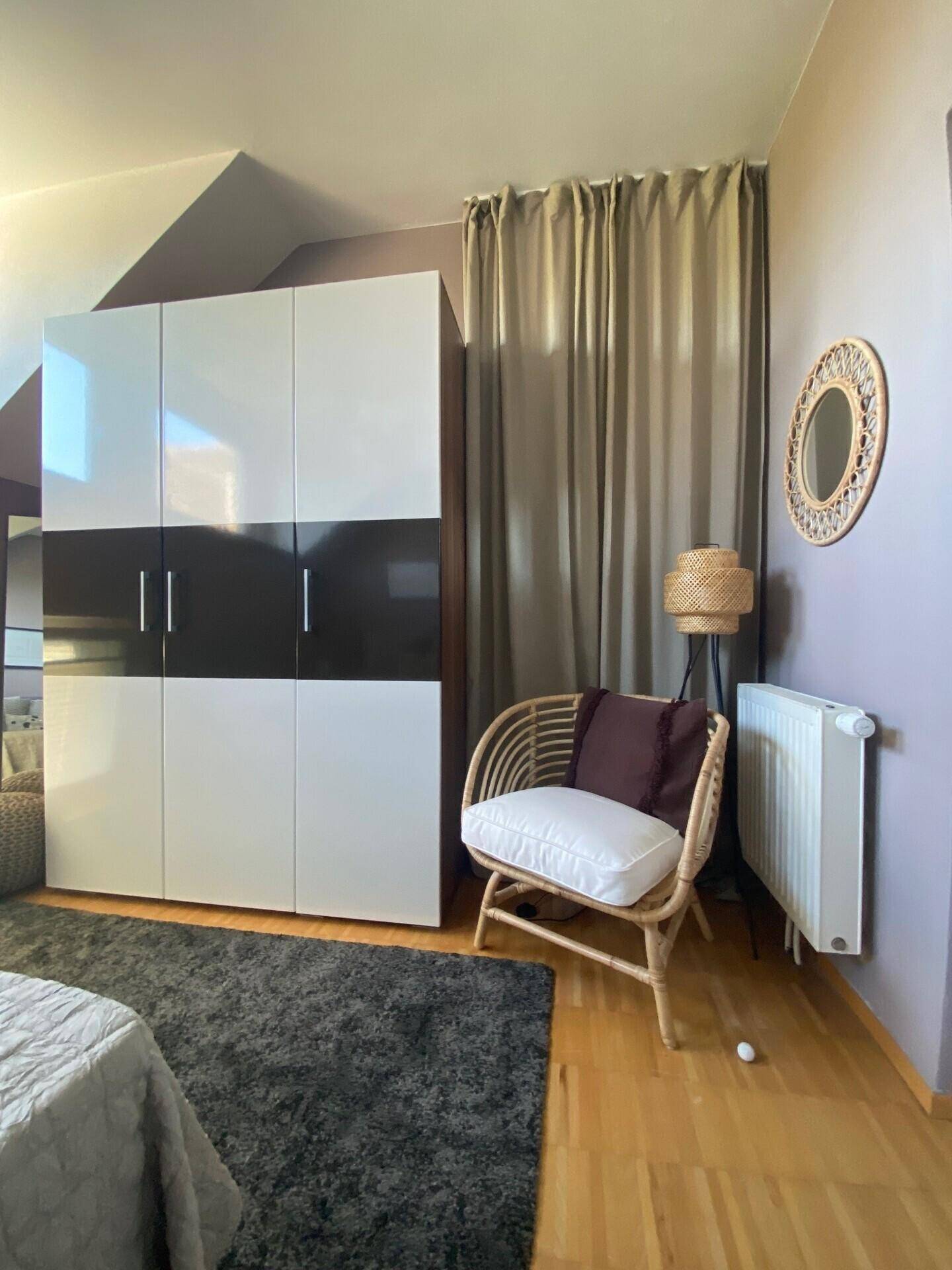 Schlafzimmer mit Holzboden, großem Kleiderschrank und einem gemütlichen Korbsessel.