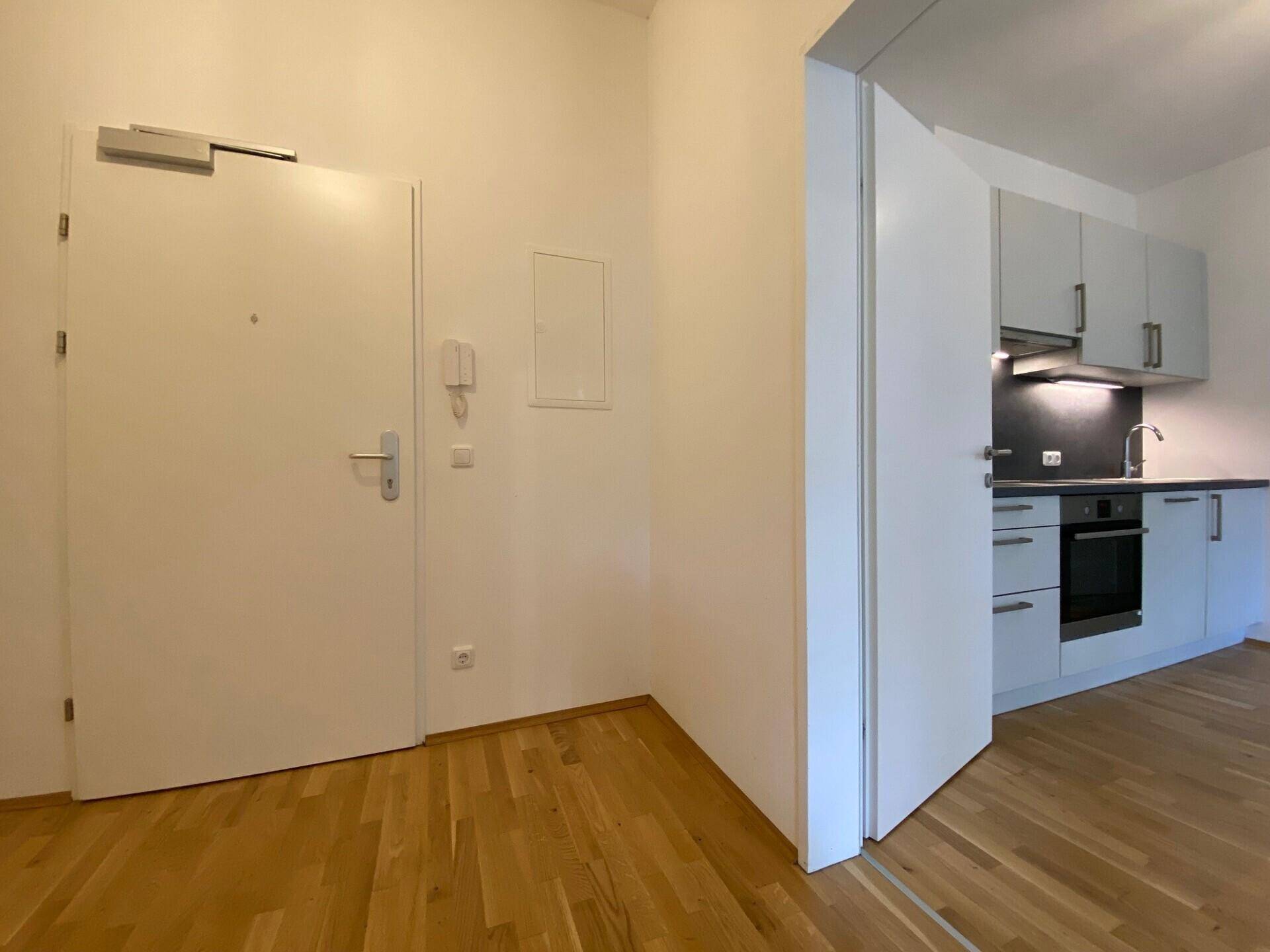 Heller Eingangsbereich mit Holzboden und Blick auf die offene Küche, inklusive Gegensprechanlage.