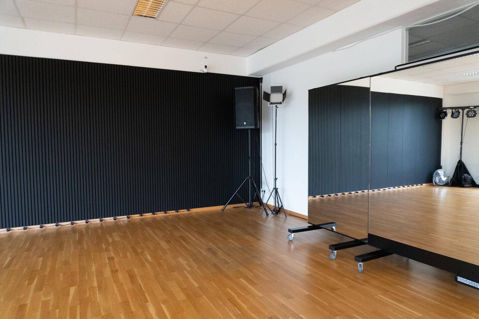 Blick auf die schwarze Akzentwand und einen großen, mobilen Spiegel im Studiobereich.