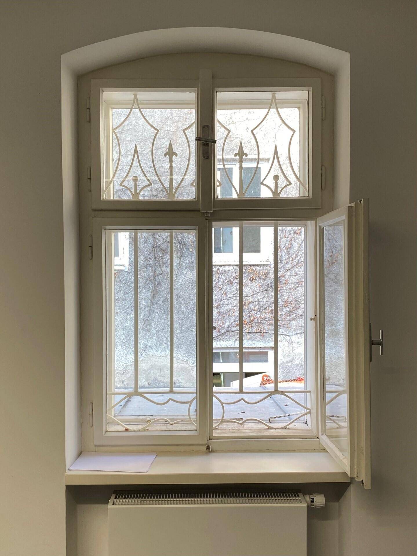 Detailansicht eines Fensters mit dekorativen Gittern und einem Heizkörper darunter.