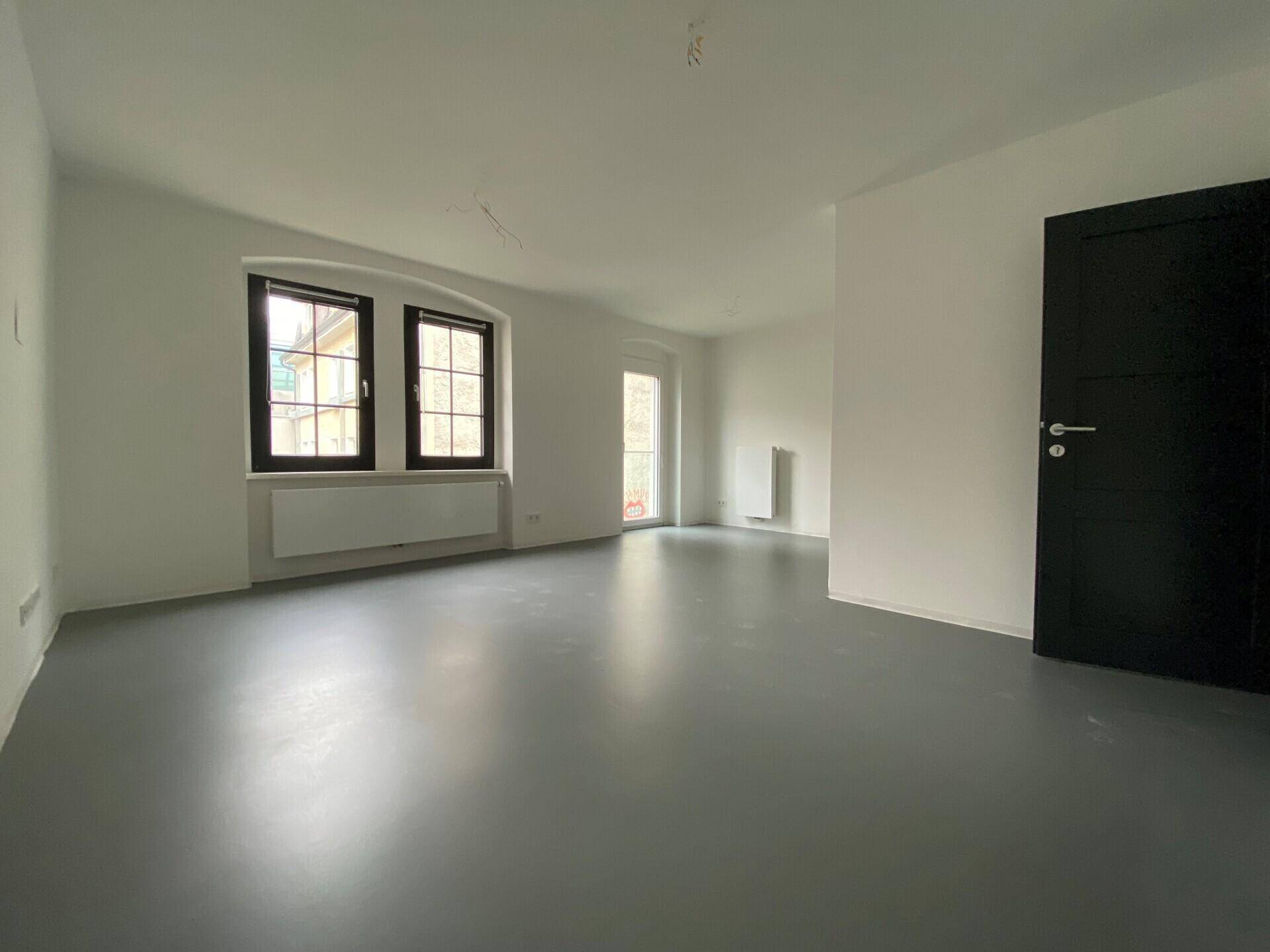Geräumiges, unmöbliertes Wohnzimmer mit großen Fenstern und hellem Boden, bereit zur Gestaltung.