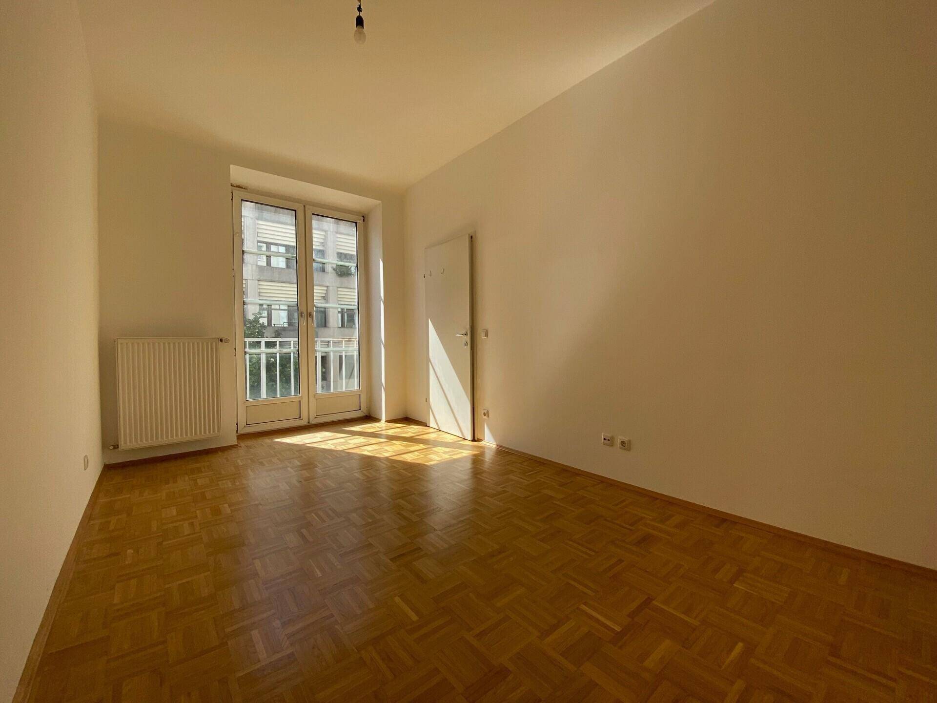 Sonniger Raum mit Parkettboden und Zugang zu einem kleinen Balkon oder einer französischen Balkontür.