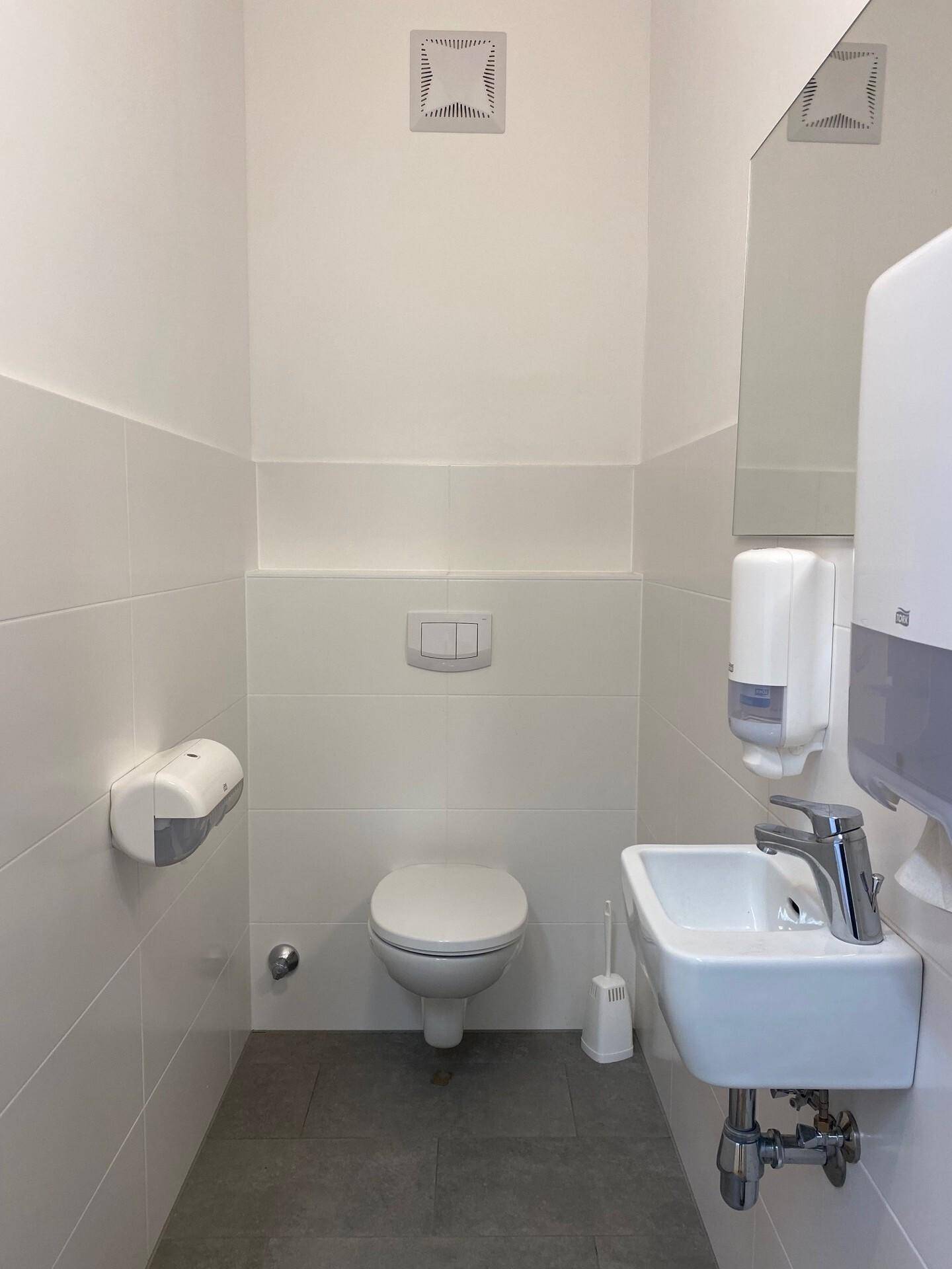 Modernes WC mit wandhängender Toilette, kleinem Waschbecken und Deckenlüfter.