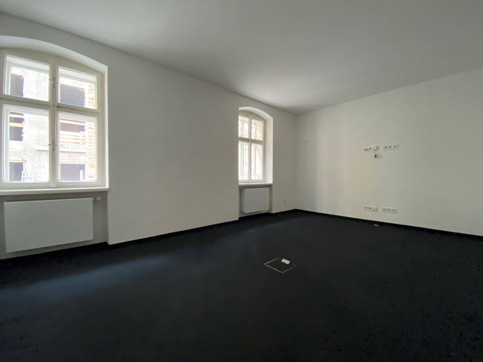 Geräumiges Büro mit dunklem Teppichboden und hohen Fenstern, ideal für Arbeitsbereiche.