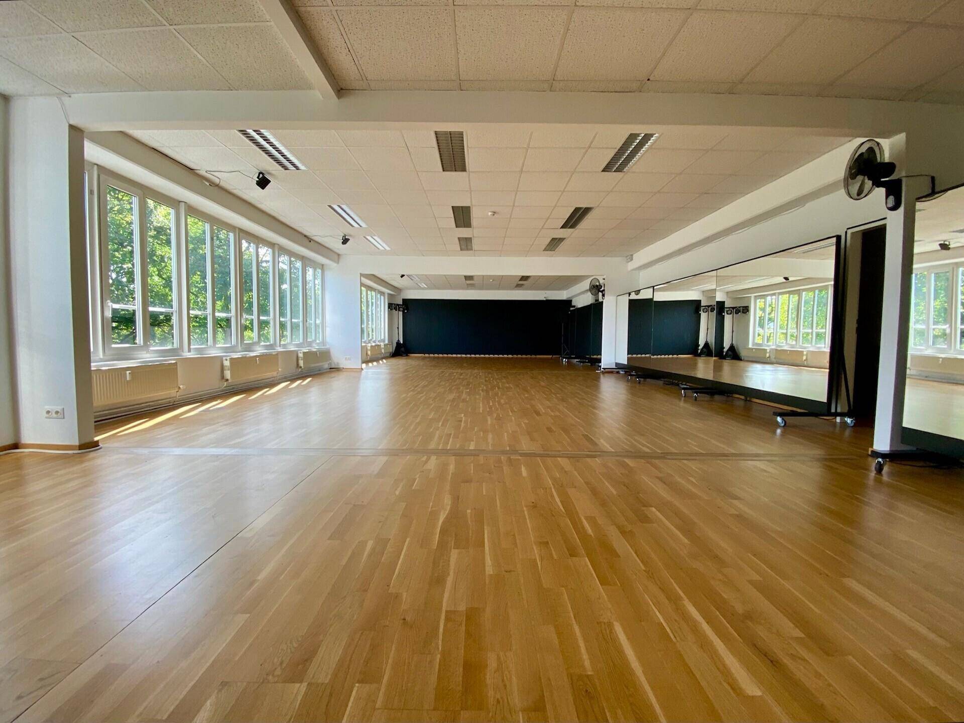 Geräumiger Studiobereich mit Holzboden, großen Spiegeln und einer schwarzen Akzentwand.