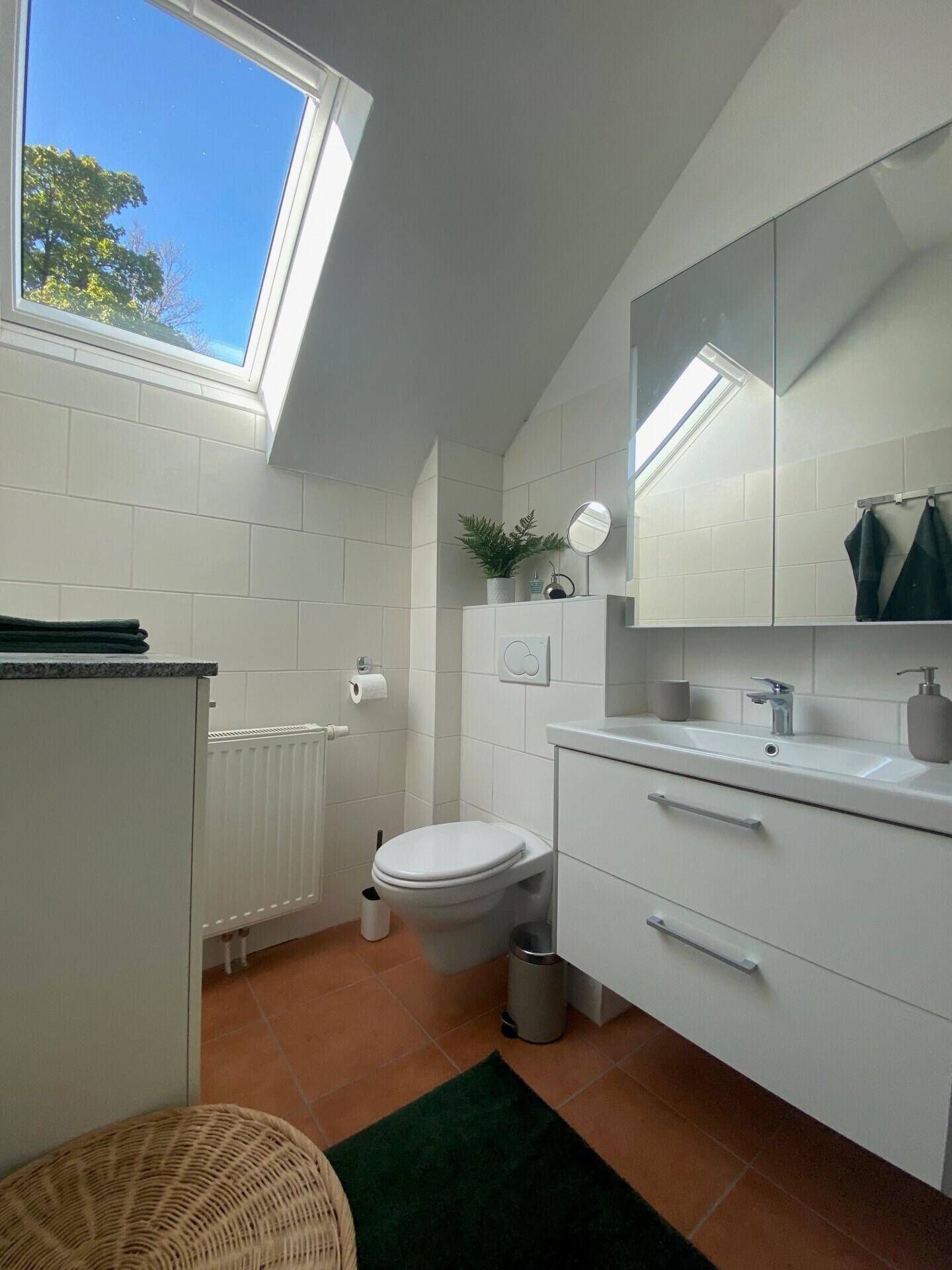 Modernes Badezimmer mit weißen Fliesen, Waschtisch und Dachfenster für natürliches Licht.