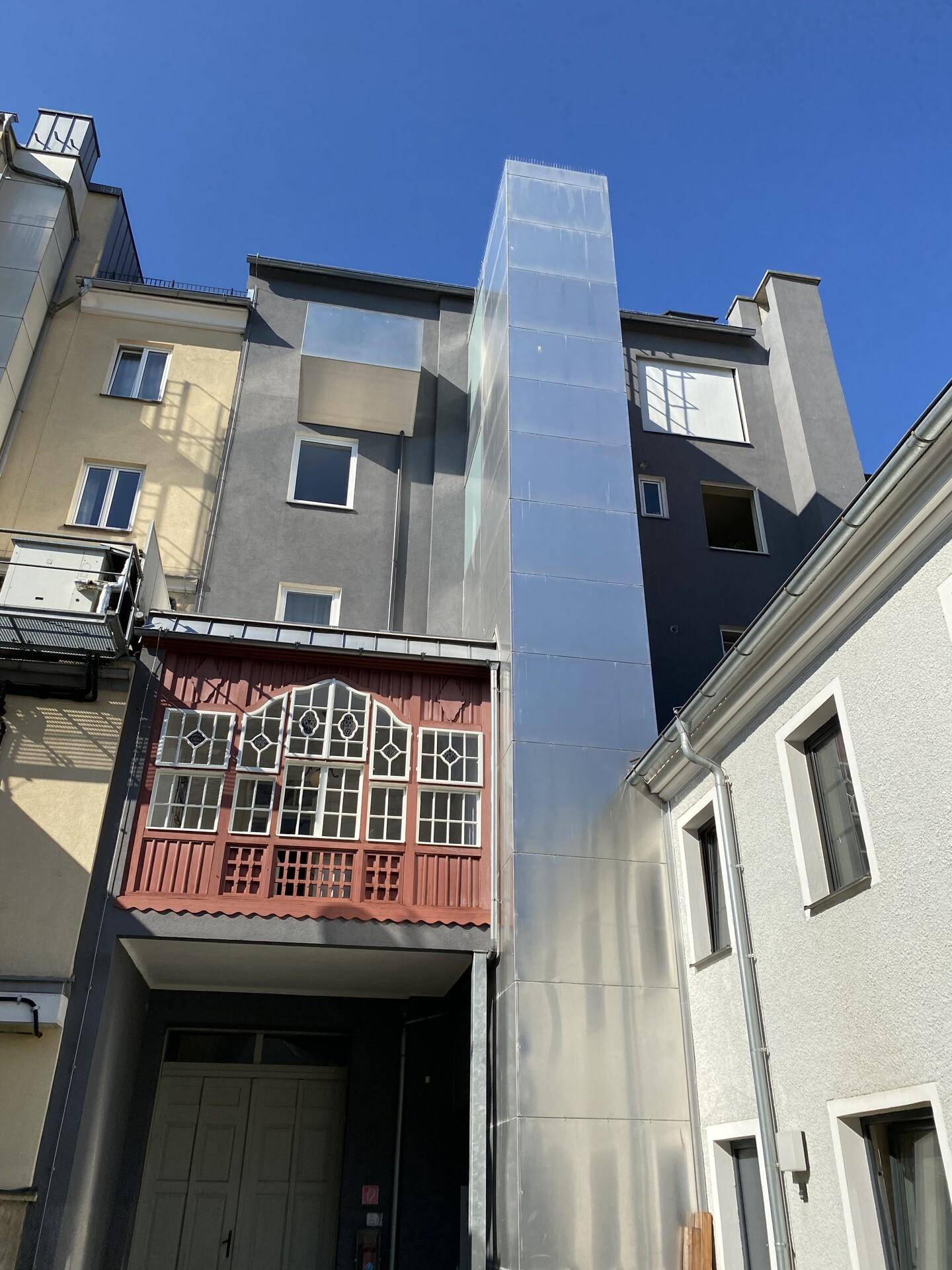 Außenansicht eines Gebäudes mit einem modernen, gläsernen Aufzugsschacht, der sich von der traditionellen Fassade abhebt.
