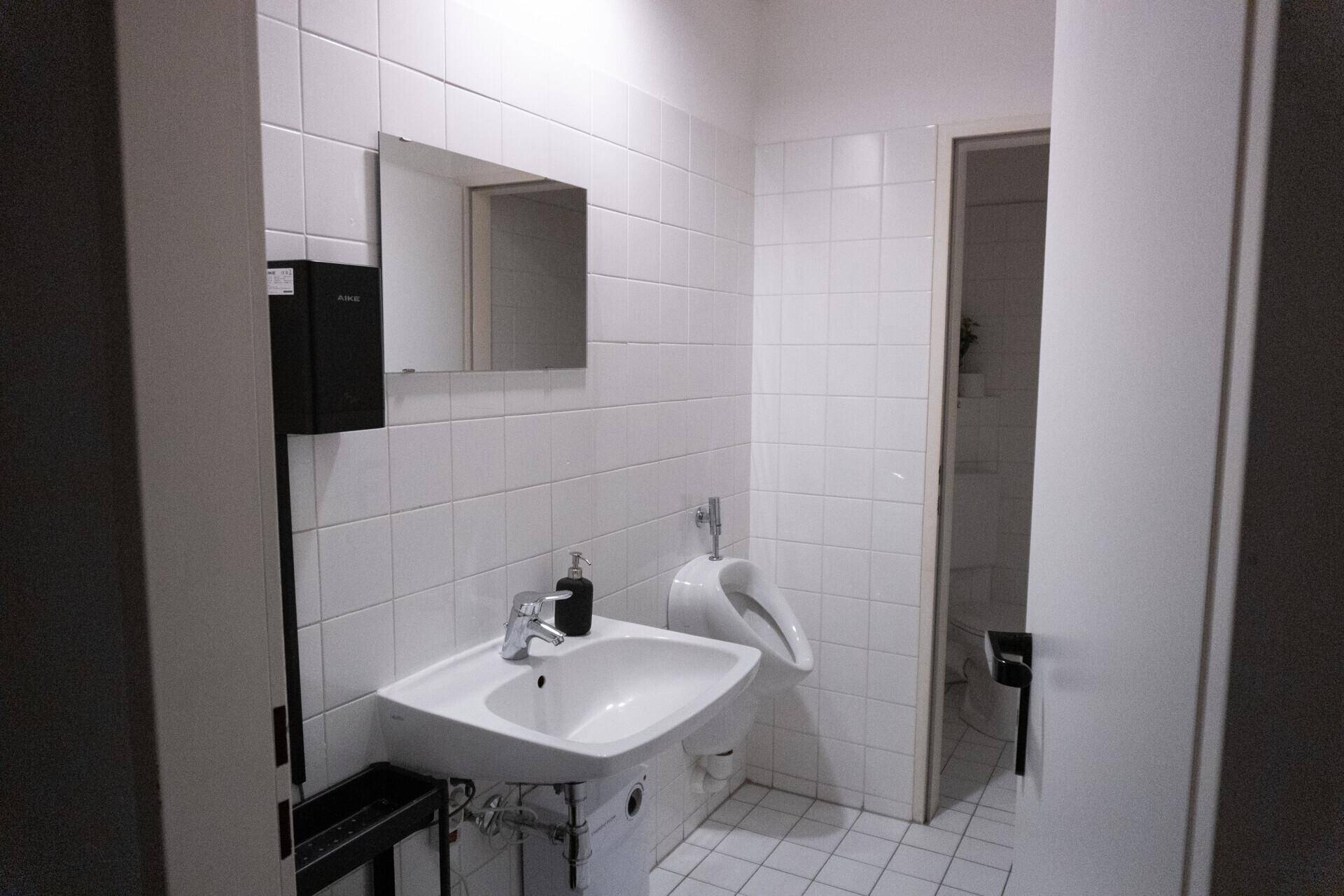 Öffentliche Toilette mit weißen Fliesen, einem Waschbecken und einem Urinal.