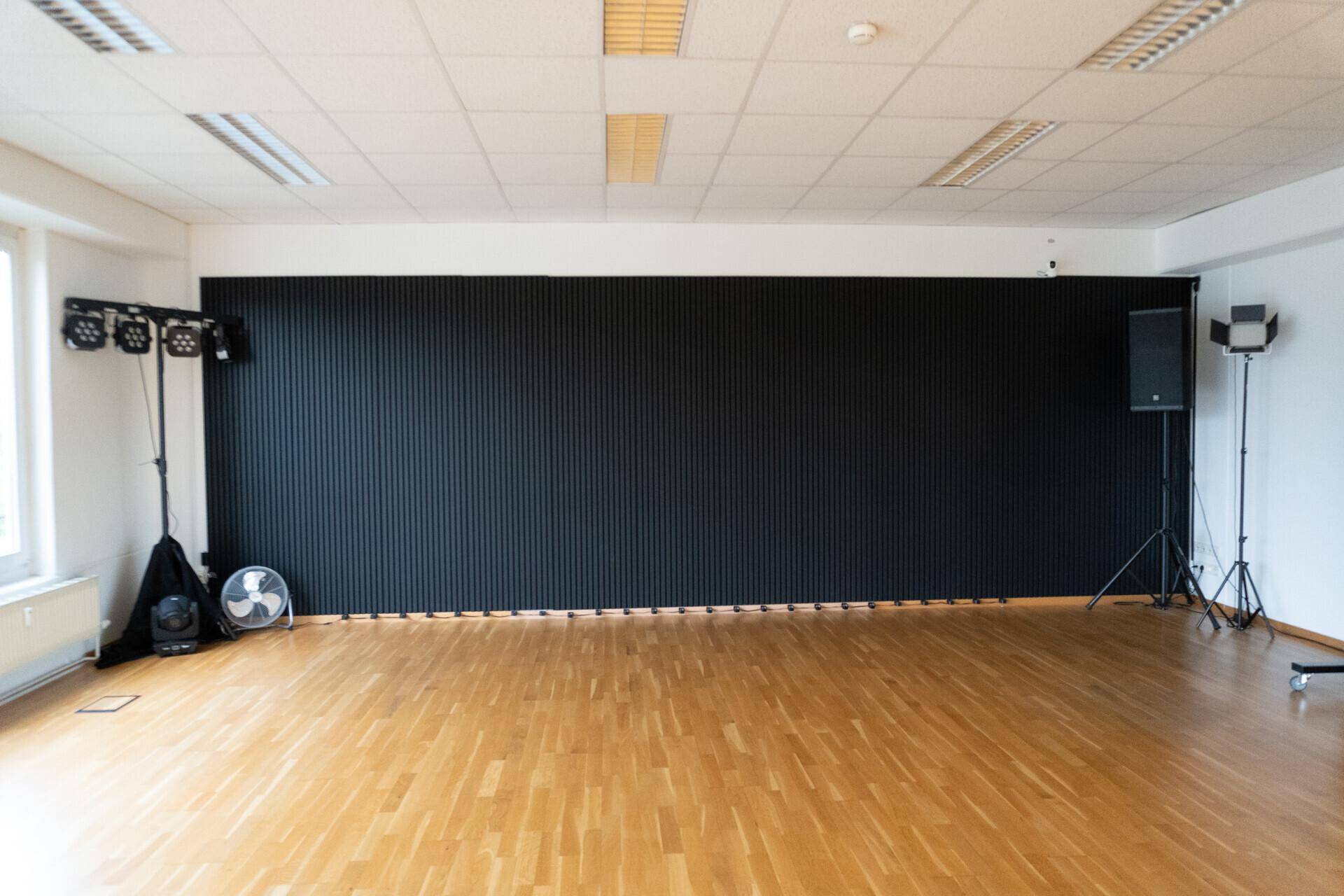Detailansicht der schwarzen Akzentwand mit gerippter Textur und professioneller Beleuchtungsausrüstung.
