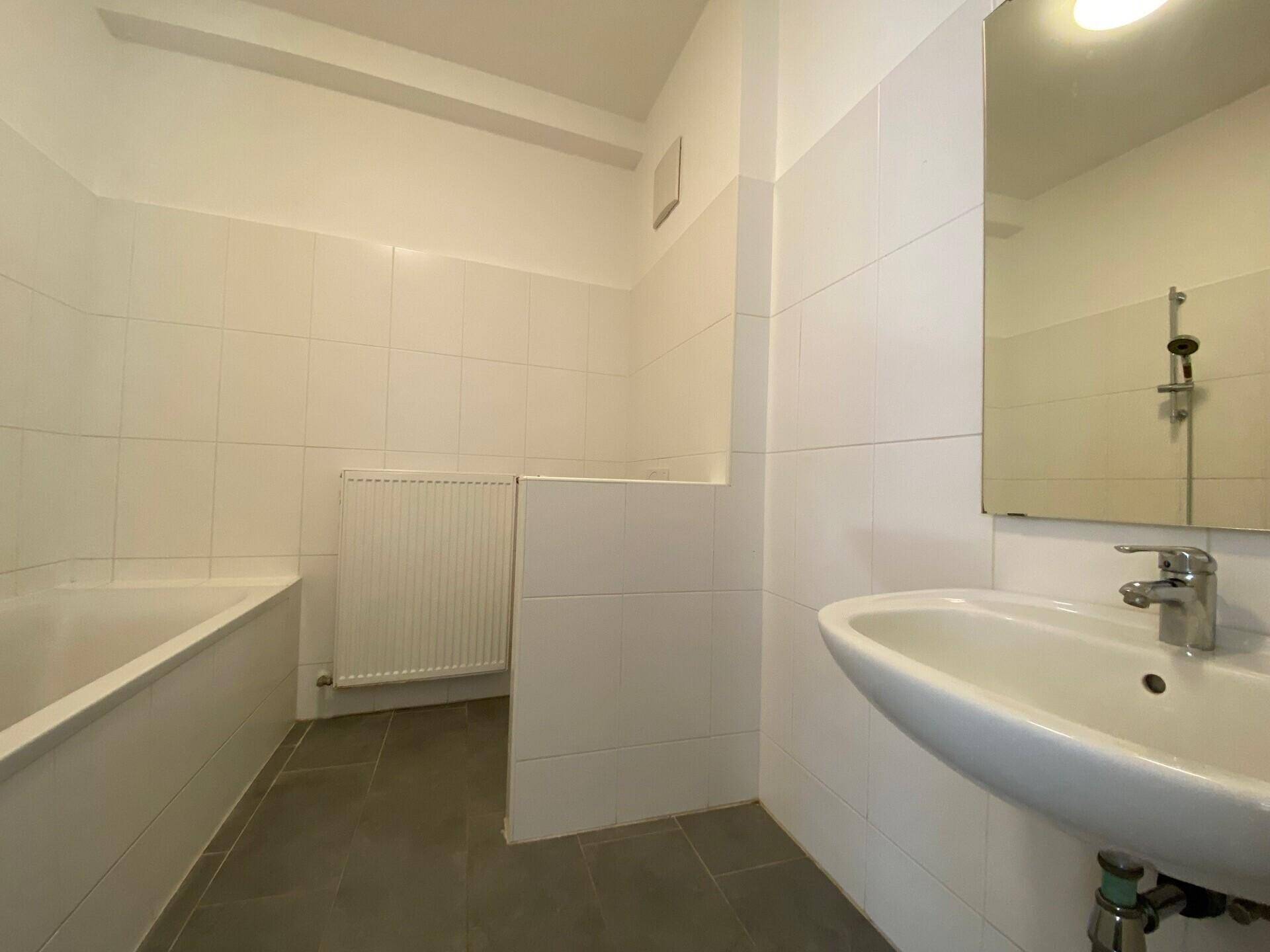 Helles Badezimmer mit weißen Wandfliesen, Badewanne und Waschbecken mit Spiegel.