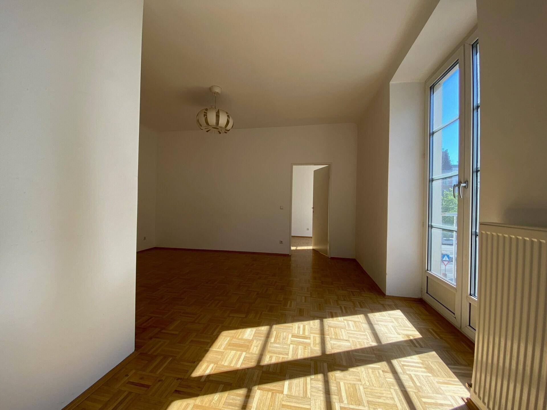 Geräumiges Wohnzimmer mit hellem Parkettboden und viel natürlichem Sonnenlicht.