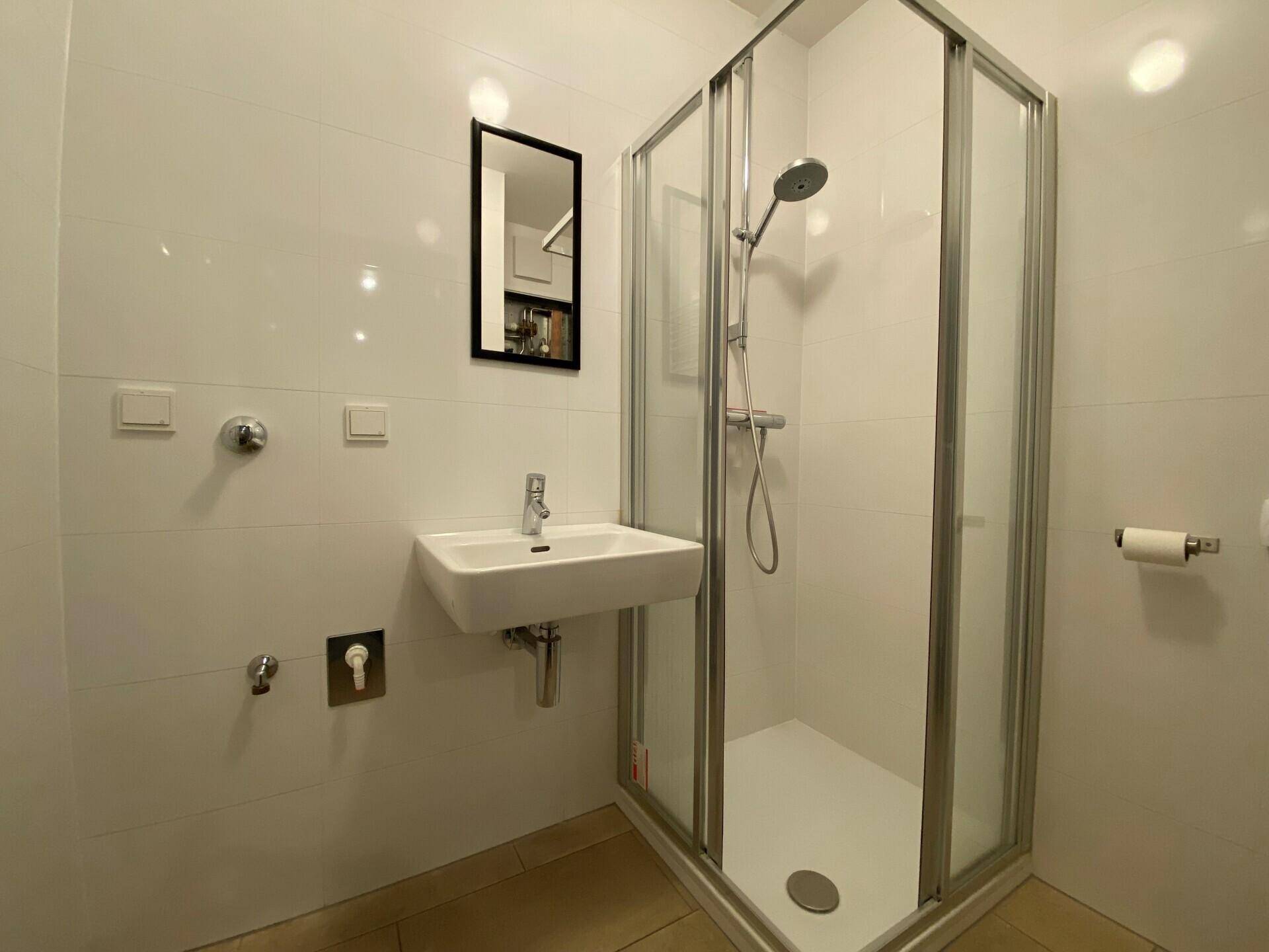 Modernes Badezimmer mit Duschkabine, Waschbecken und weißen Fliesen an den Wänden.