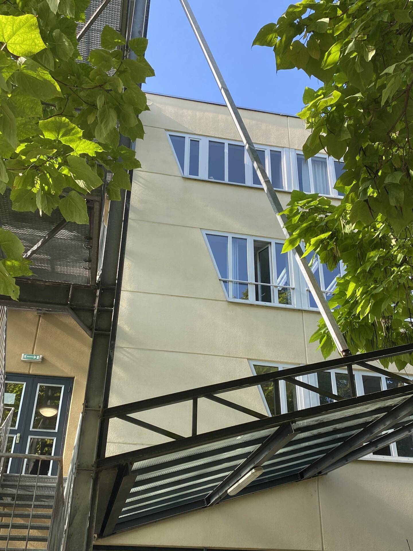 Fassade eines modernen Gebäudes mit vielen Fenstern und umgebenden Bäumen.