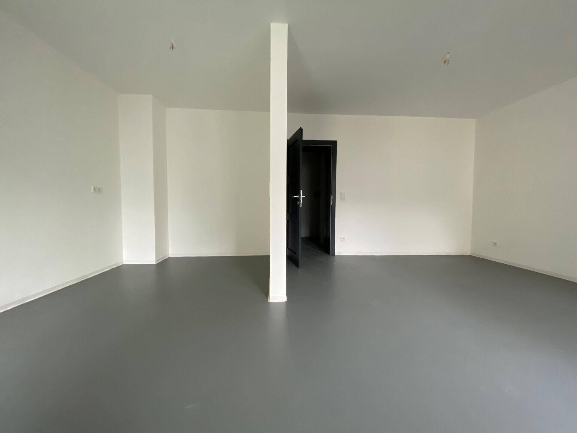Großer, leerer Raum mit weiß gestrichenen Wänden und einem modernen grauen Bodenbelag.